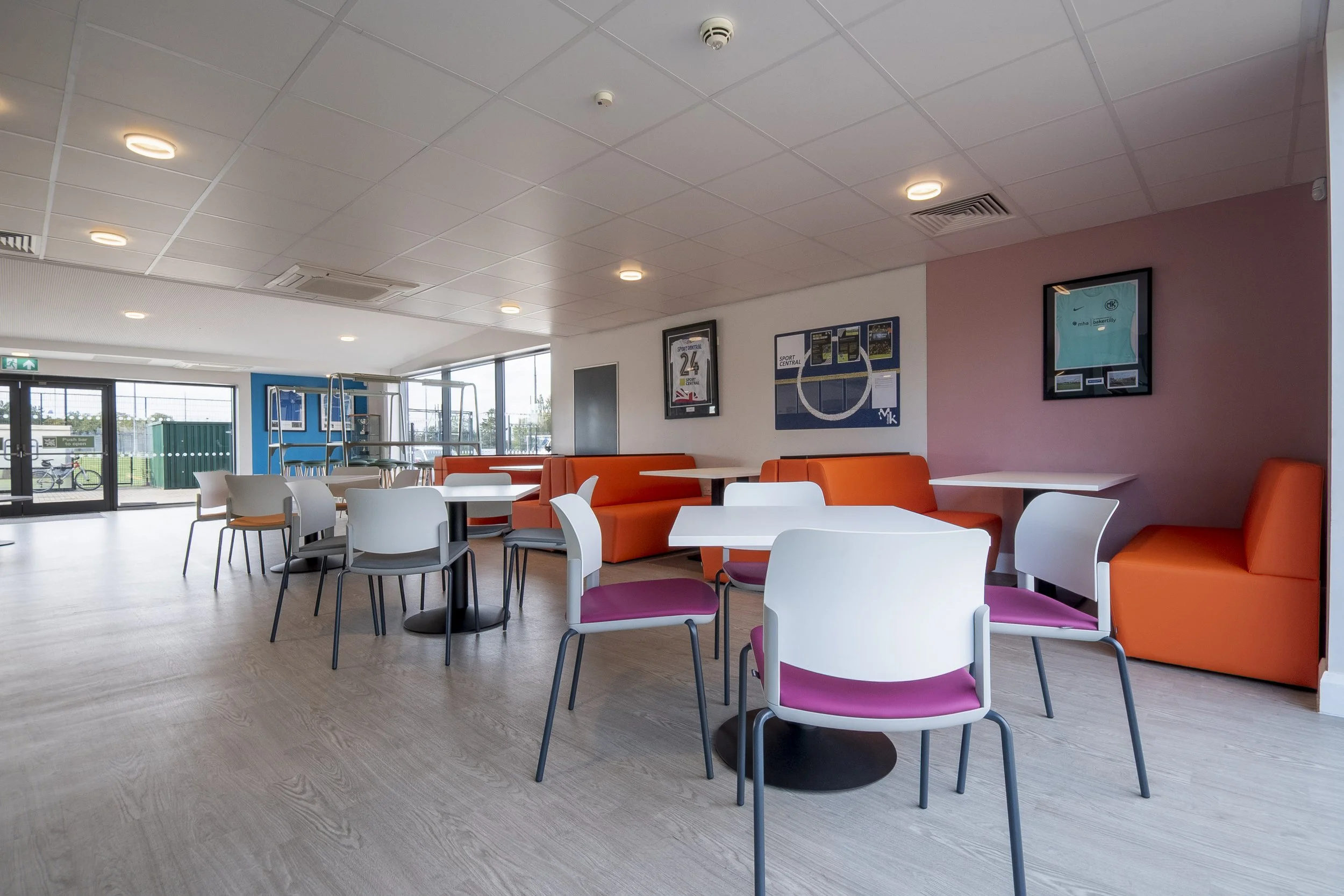 Café seating with pink-seat chairs and an orange booth in a bright room
