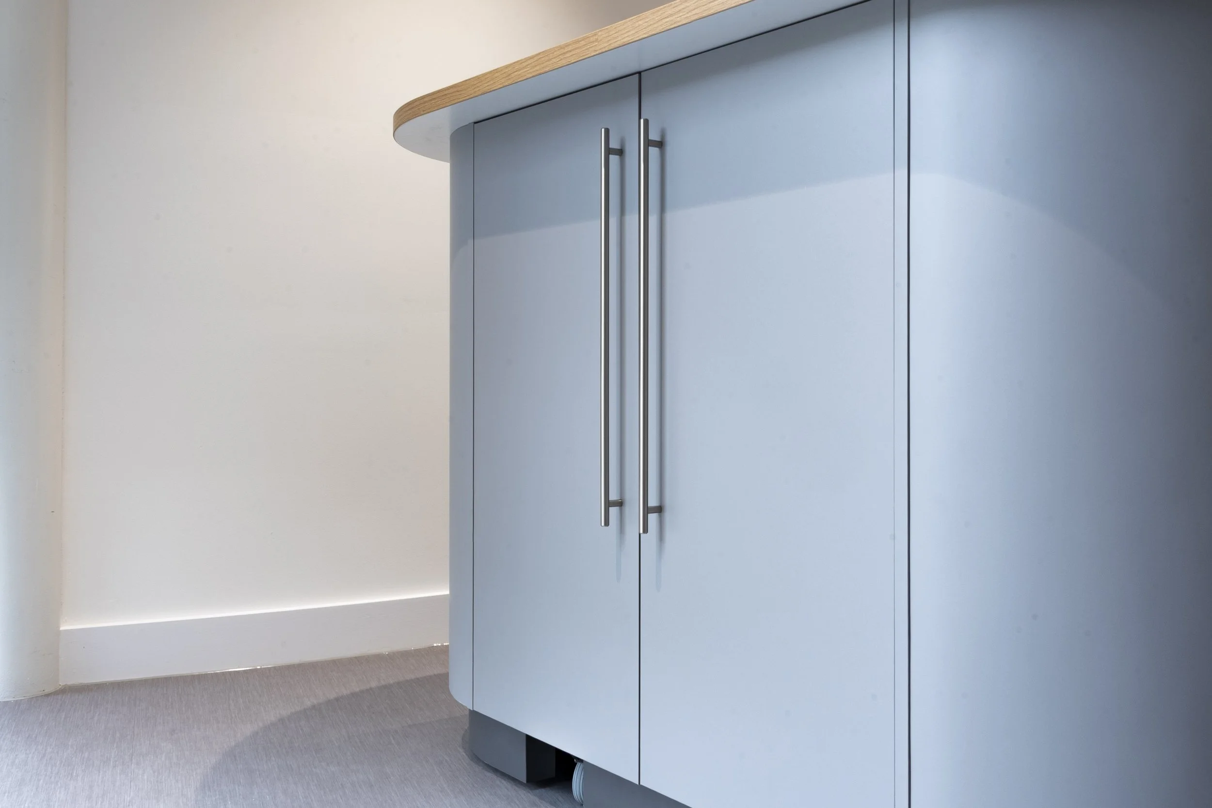 Close-up of a curved blue-grey cabinet with steel handles and a timber top