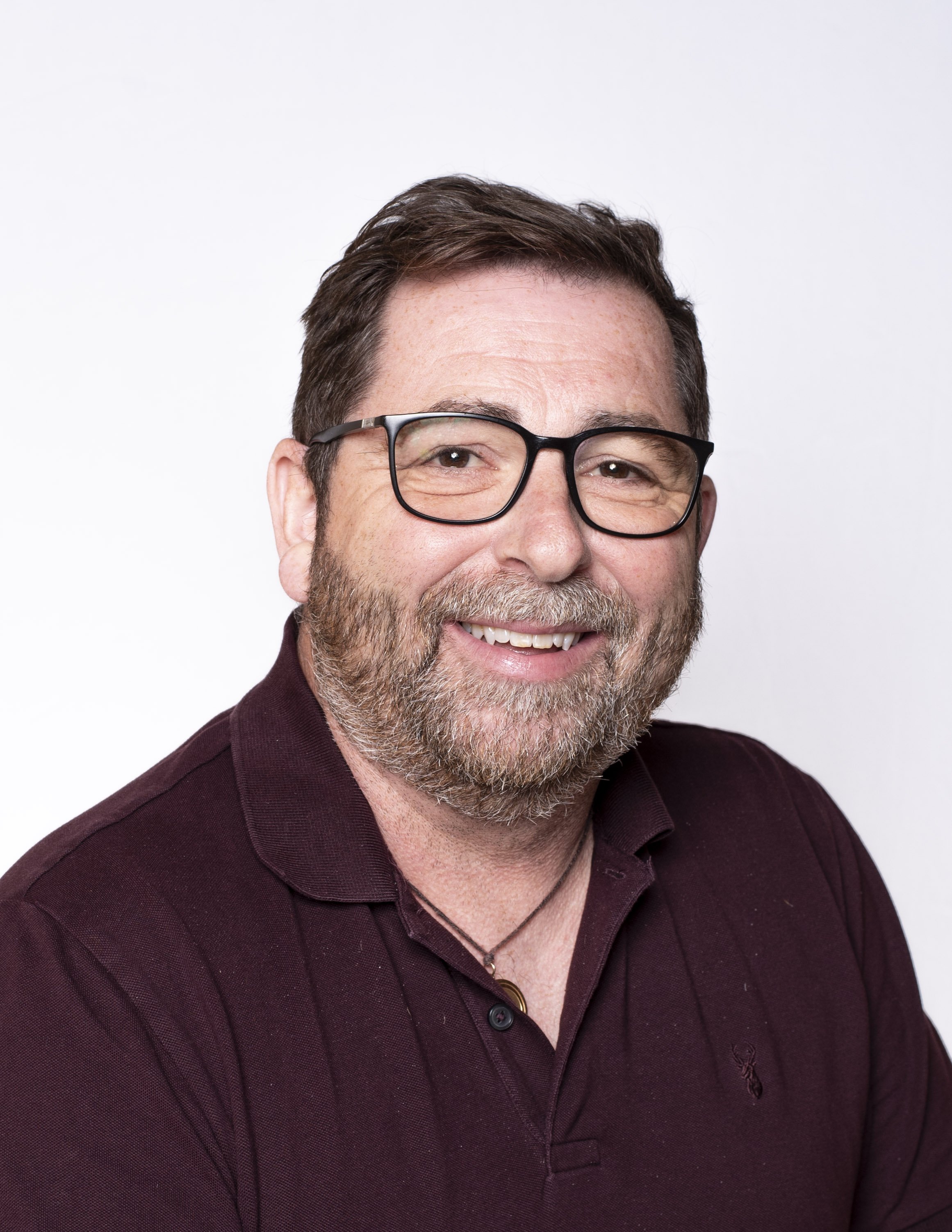 Closer headshot of a smiling man with glasses and a beard in a burgundy polo shirt