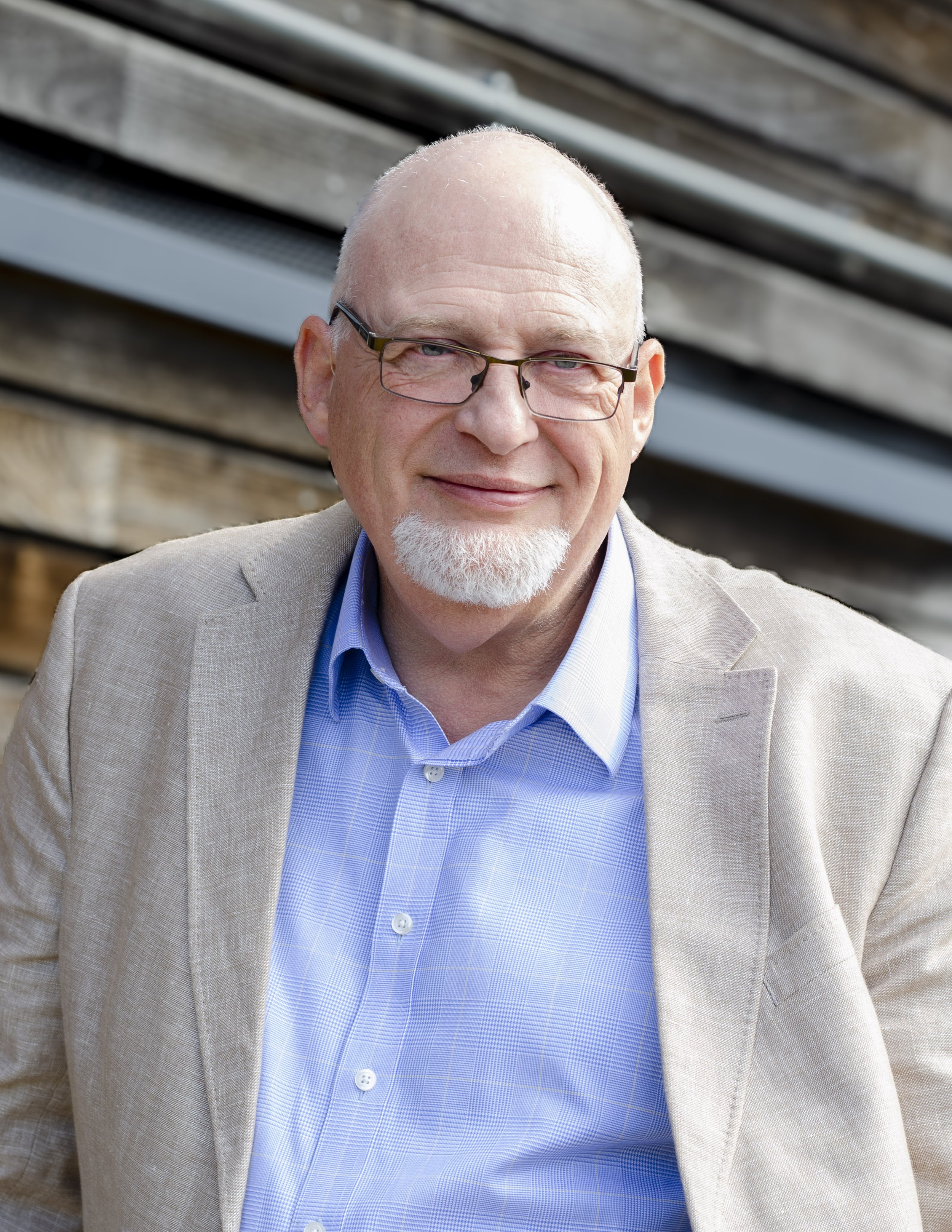 Mark Spence in a grey blazer and blue shirt in front of dark timber cladding