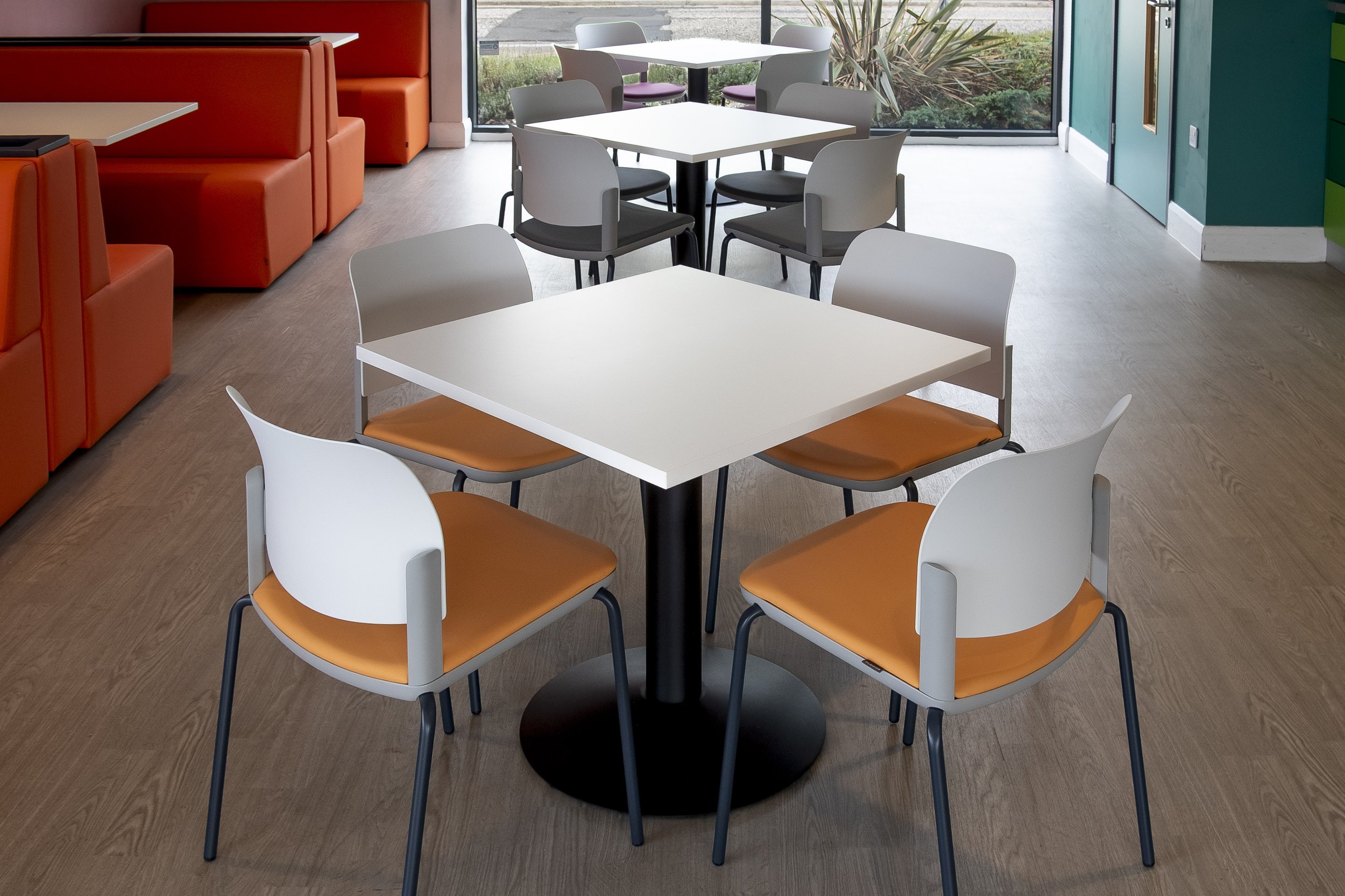 White square table with white and orange chairs in front of orange booths