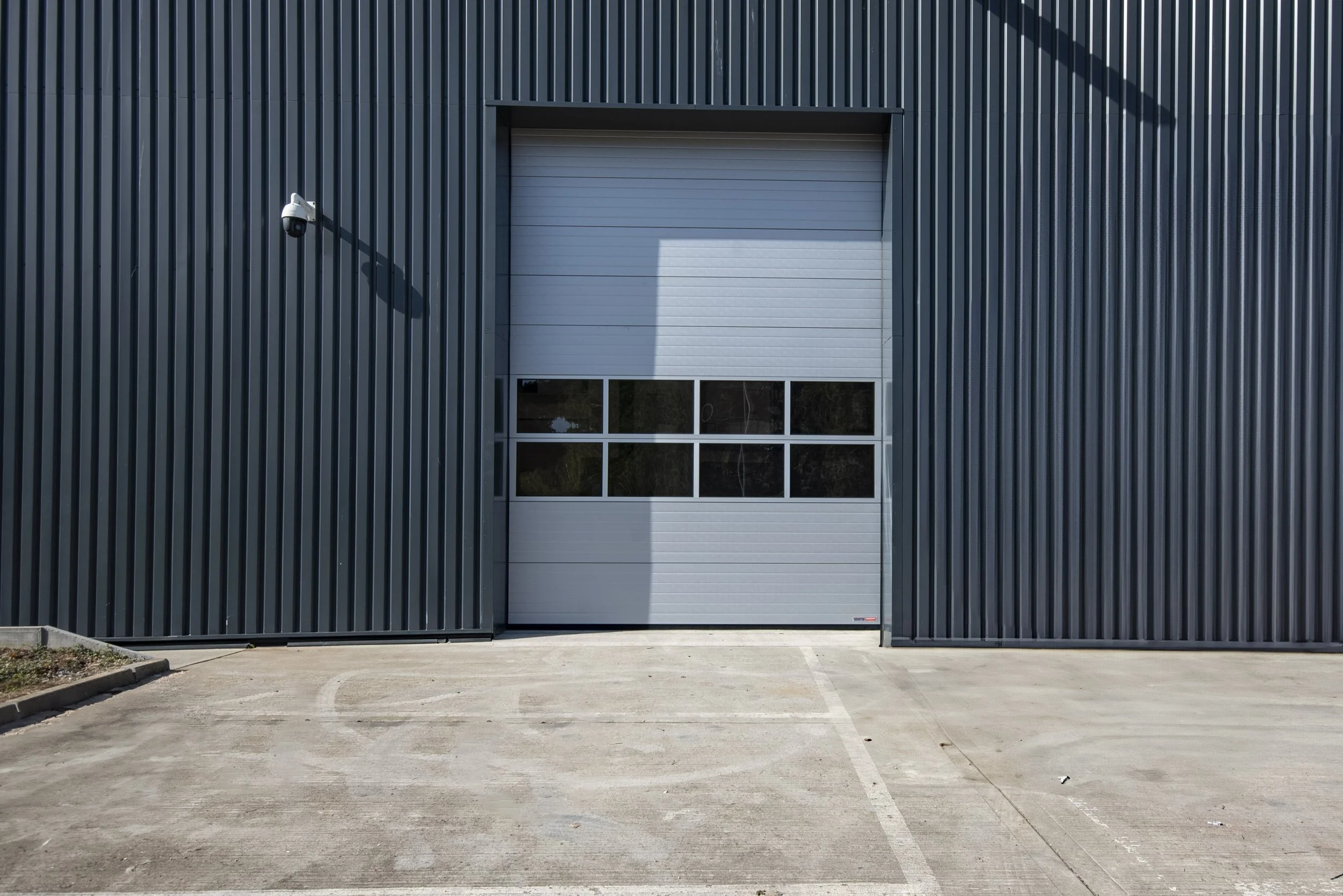 Dark grey clad warehouse building with a roller shutter door