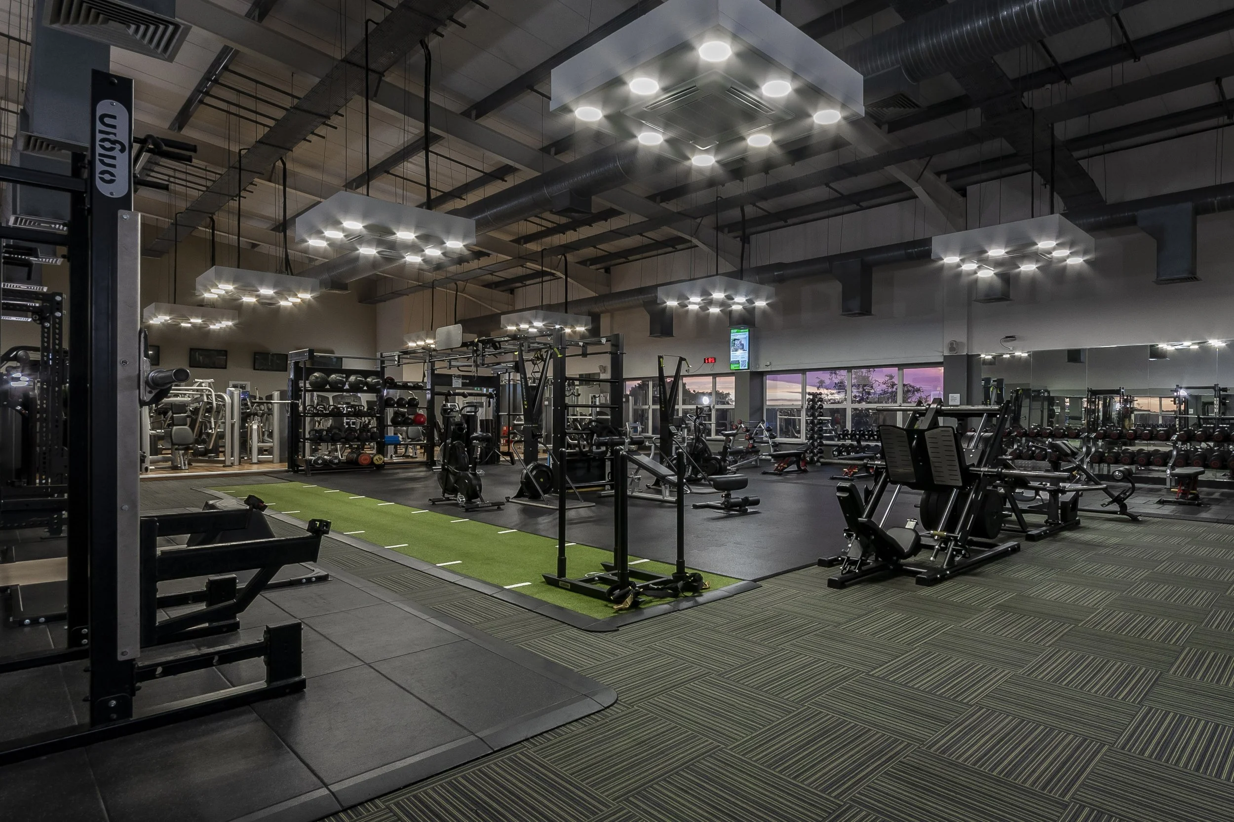 Gym floor with weight machines and a training rig under ceiling lights