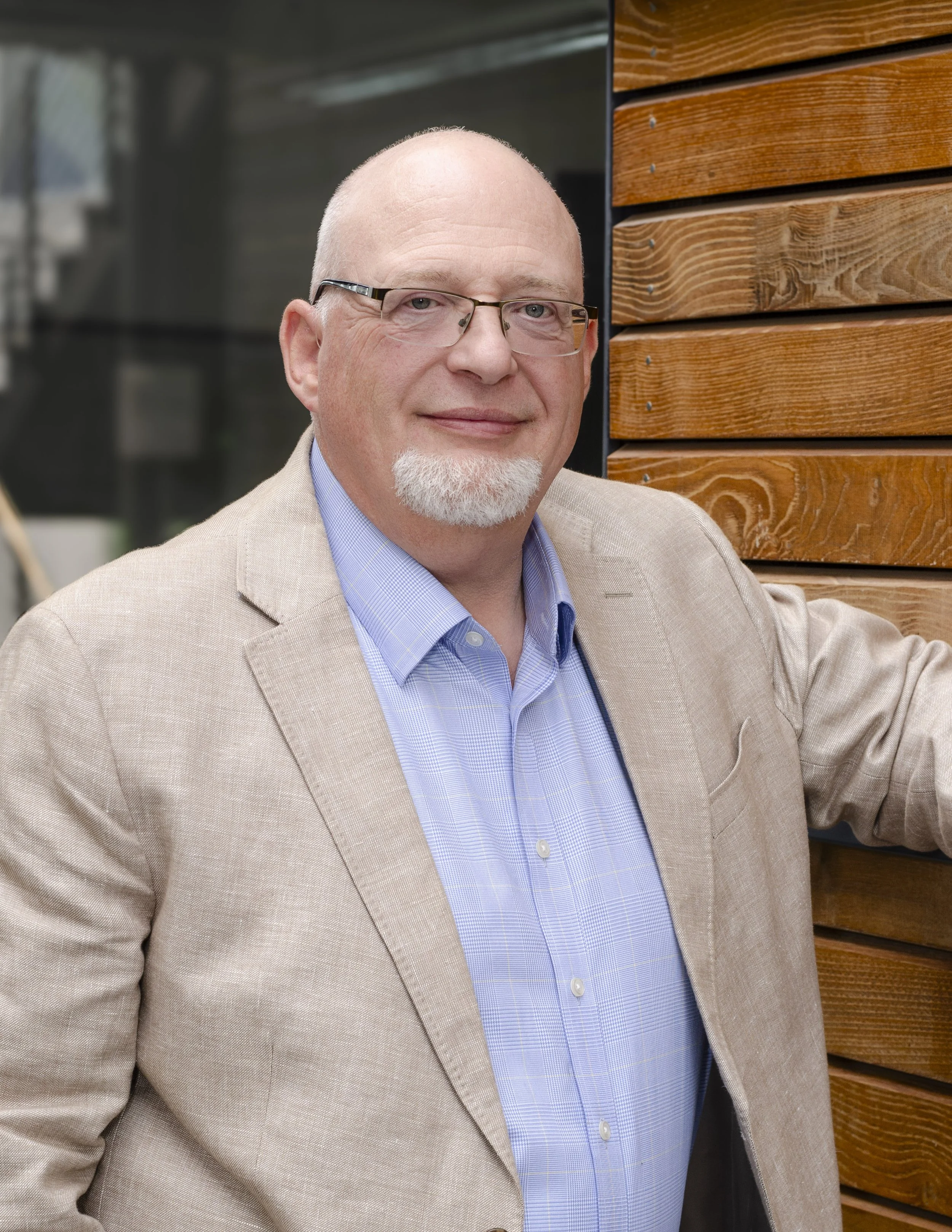 Mark Spence in a beige blazer and blue shirt standing in front of a timber wall