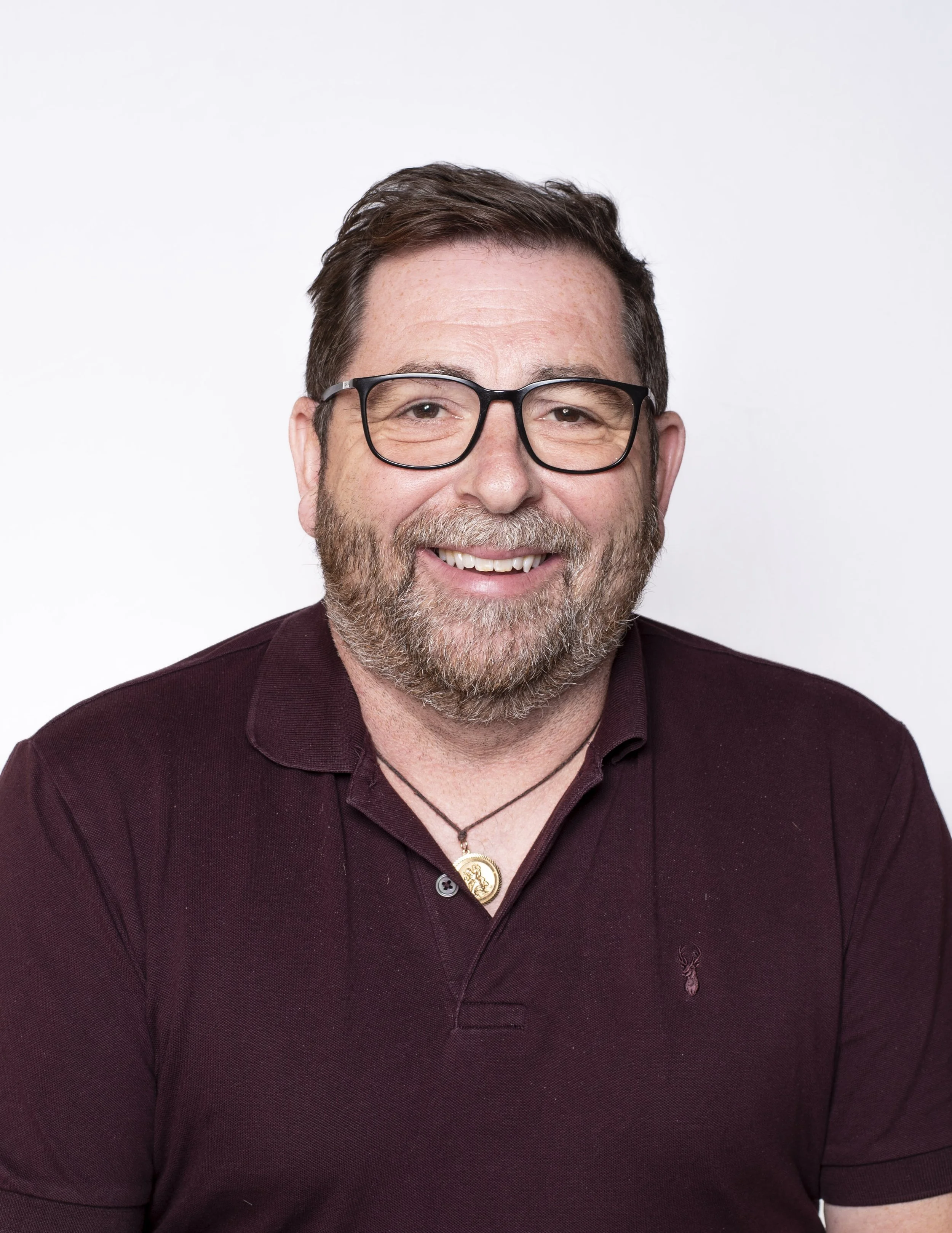 Headshot of a smiling man with glasses and a beard in a burgundy polo shirt on a white background