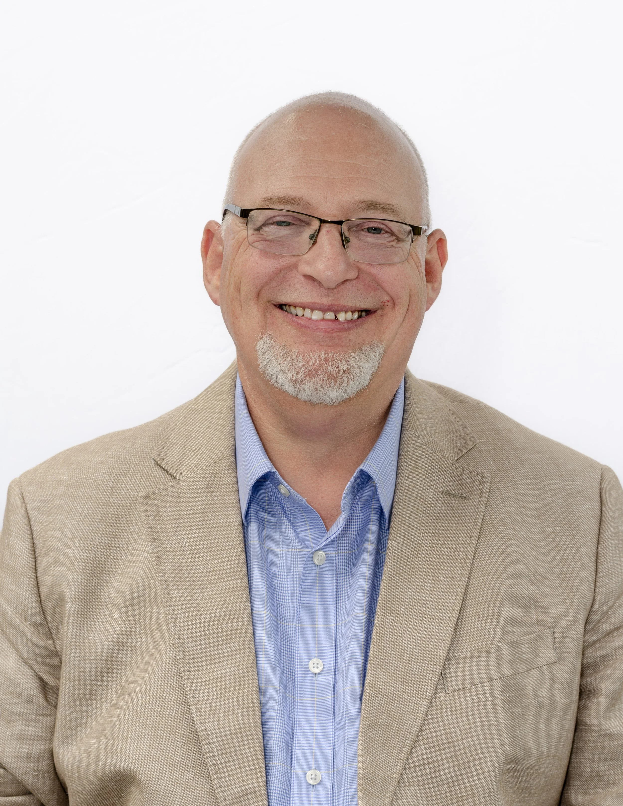 Mark Spence smiling in a beige blazer and blue shirt on a white background