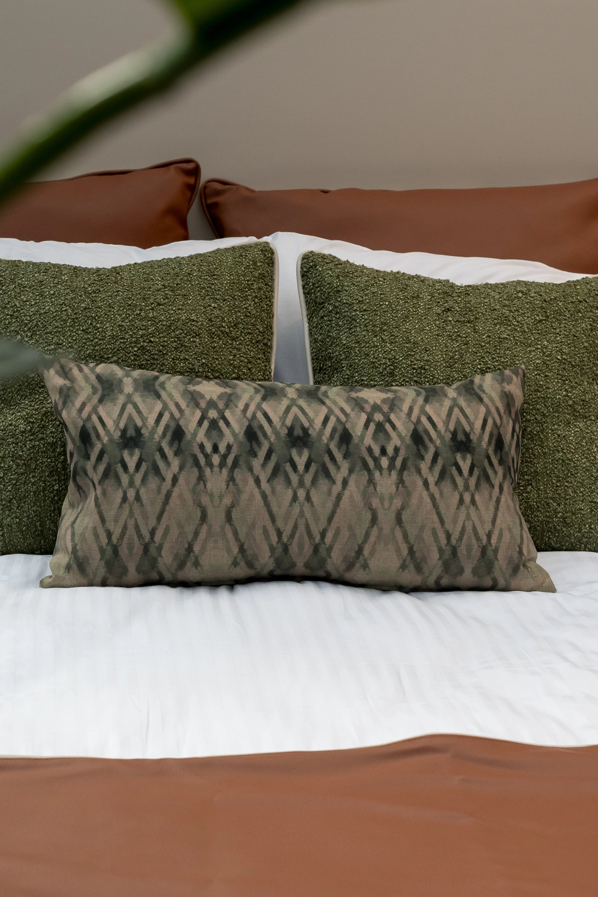 Green and tan patterned cushions on a terracotta bed_Mass Interiors