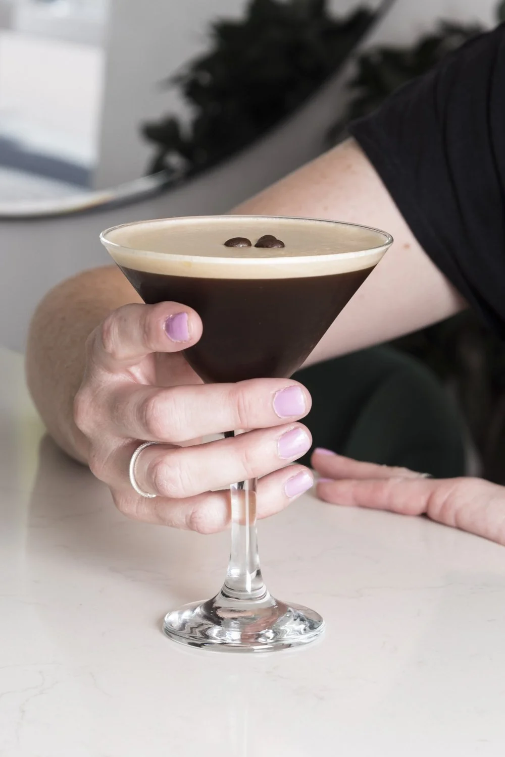 A person holding a martini glass filled with a layered coffee cocktail, topped with two coffee beans.