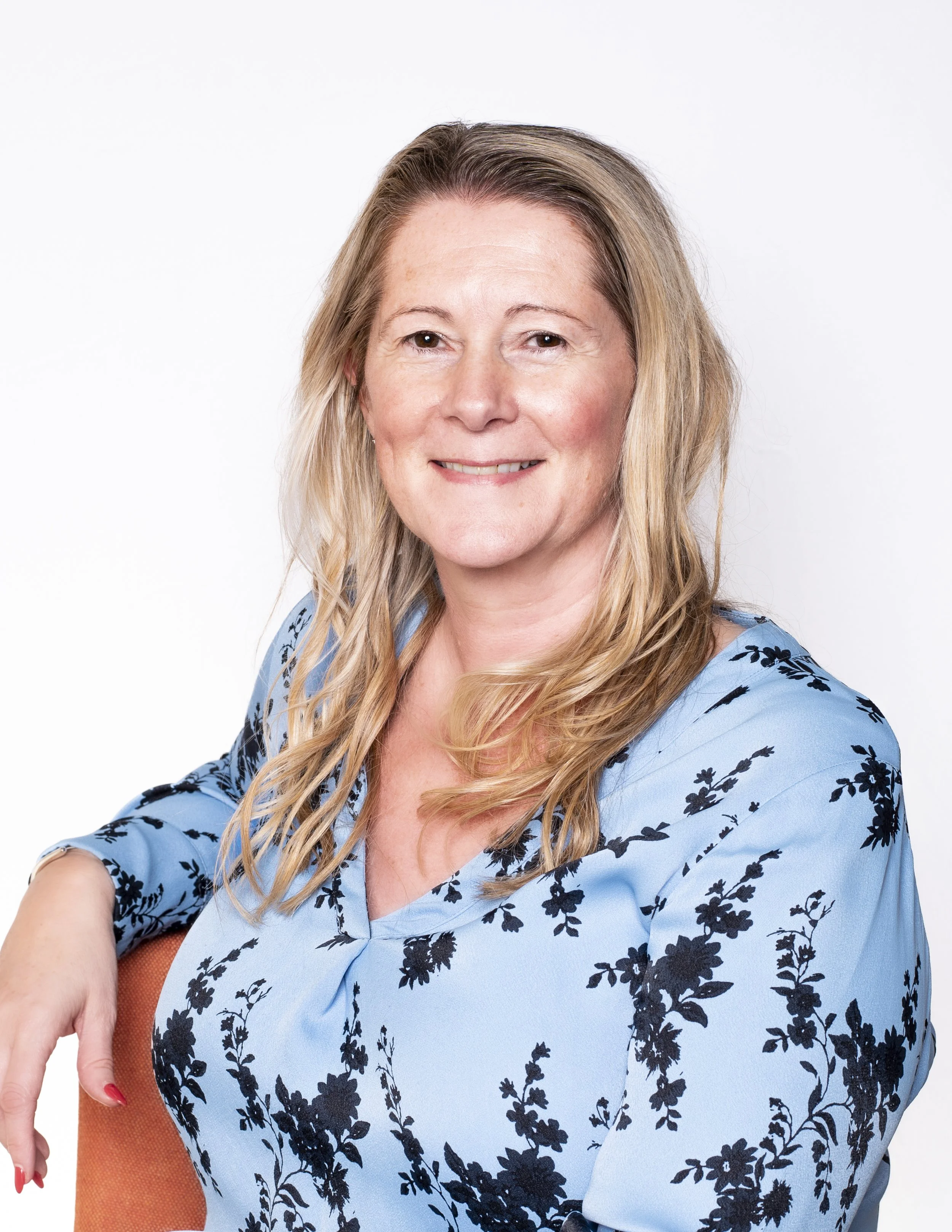 Smiling woman with long blonde hair in a blue floral blouse on a white background