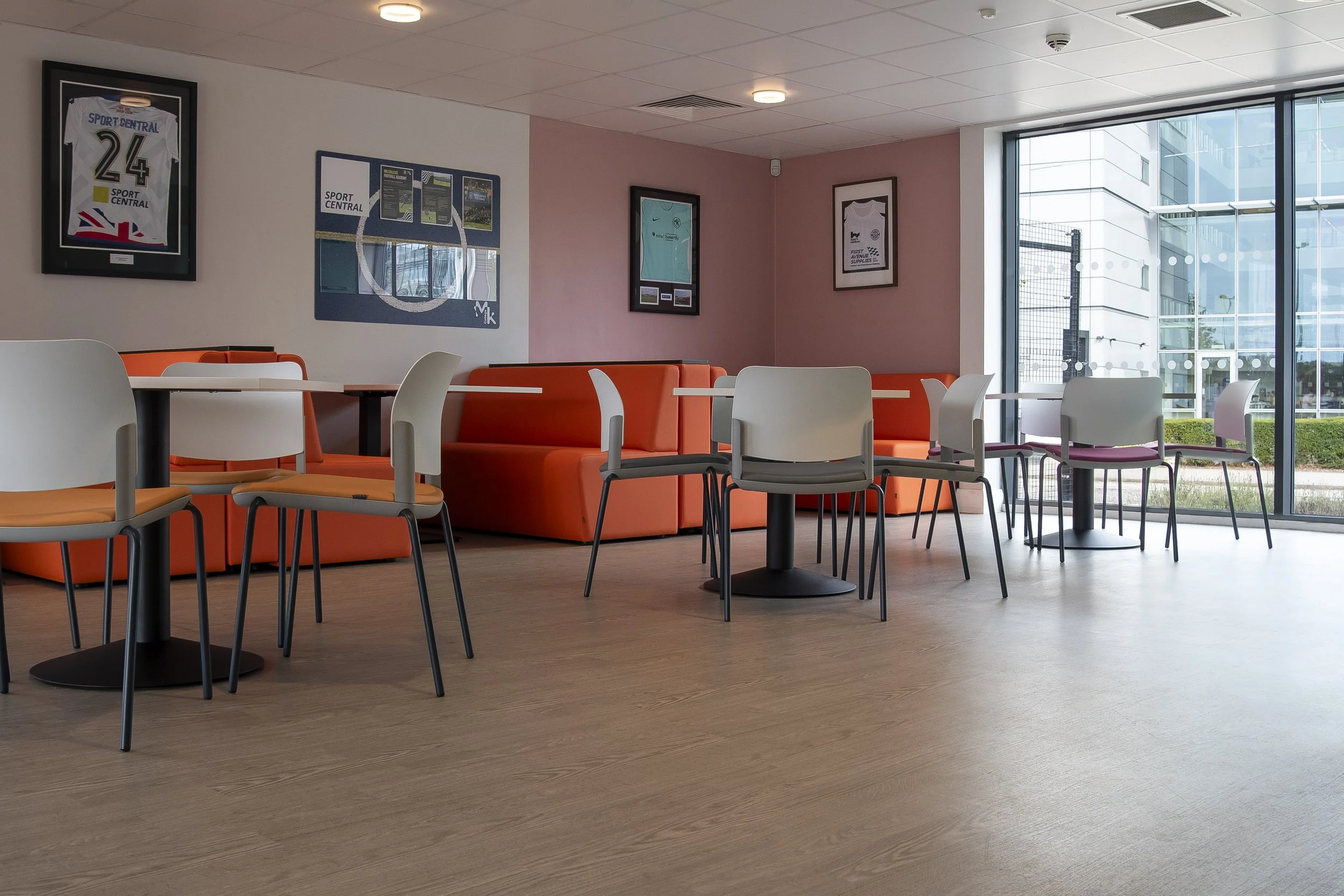 Café area with white tables, chairs and orange booths beside large windows