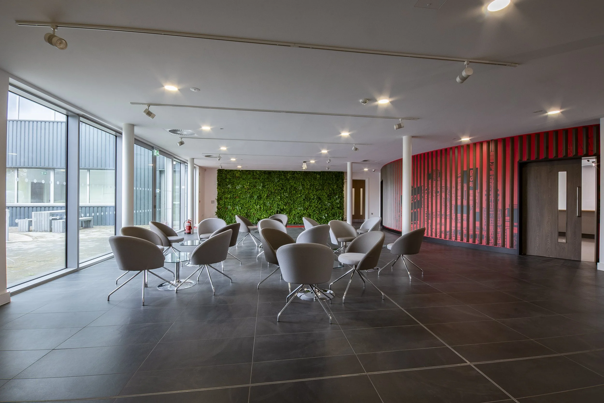 Reception break-out area with grey chairs, a moss wall and a red slatted wall