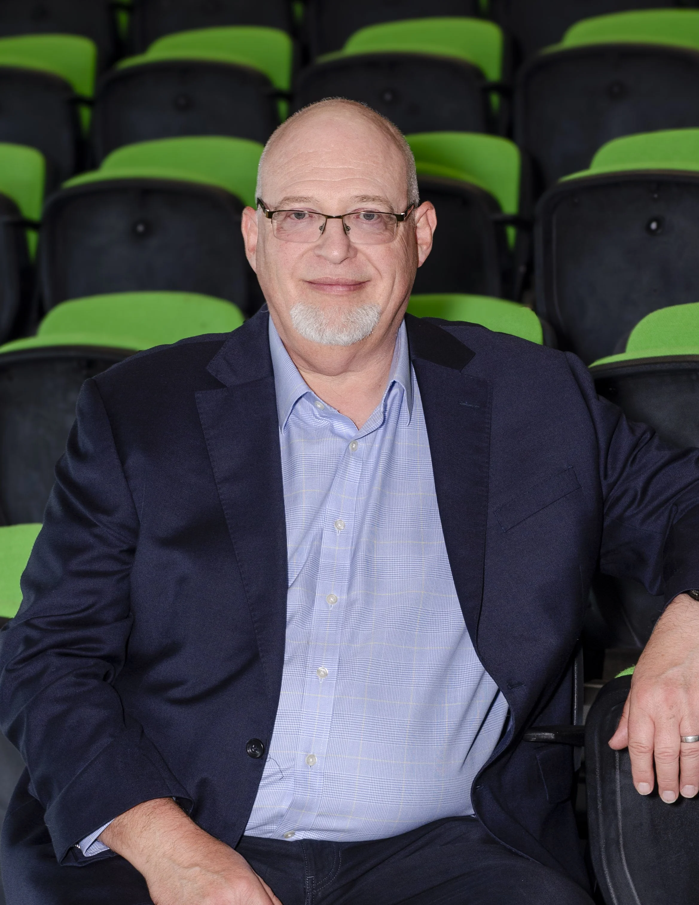 Mark Spence seated in a navy blazer among green auditorium seats