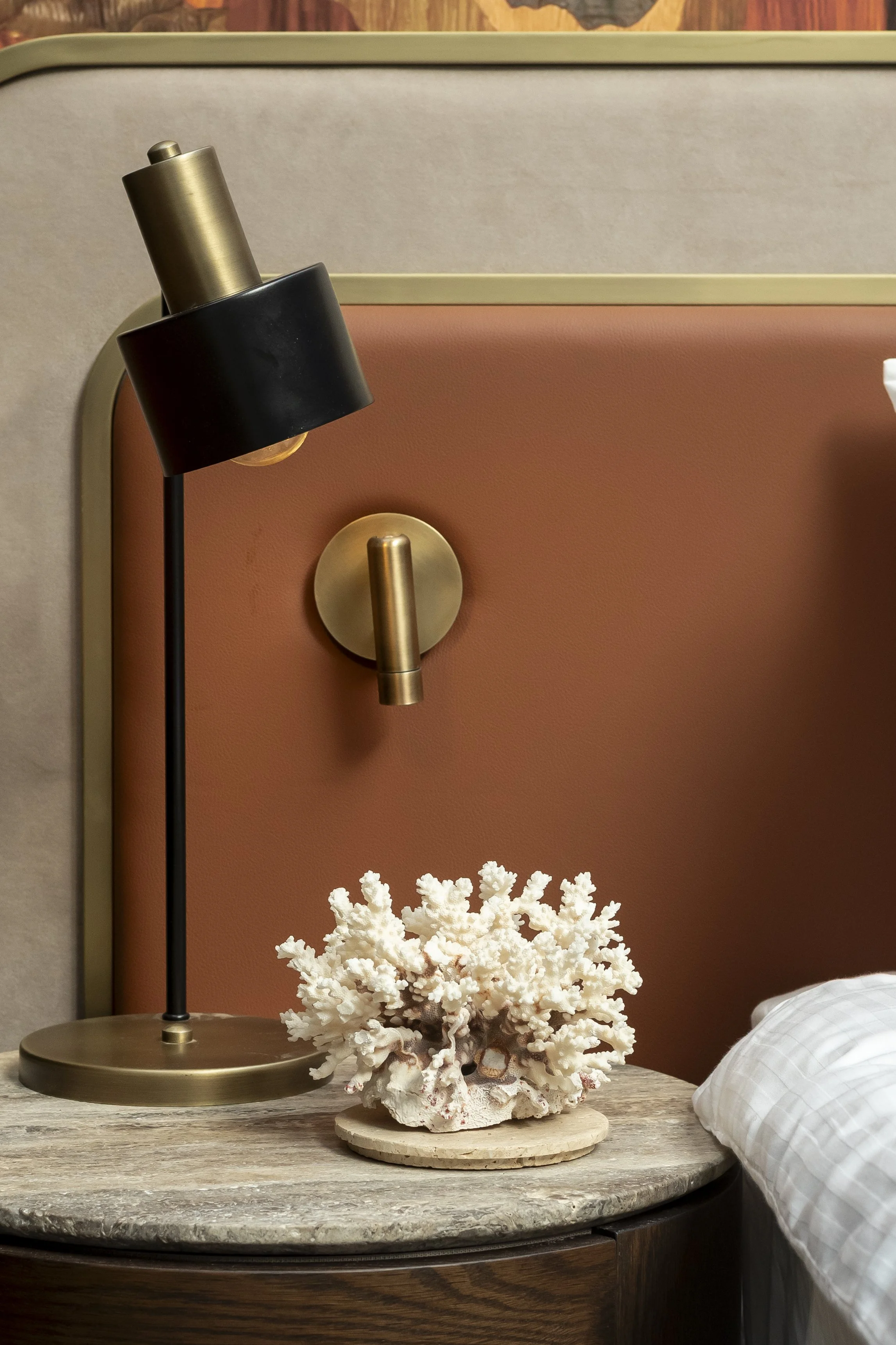 Brass wall lamp beside a coral ornament on a terracotta headboard_Mass Interiors