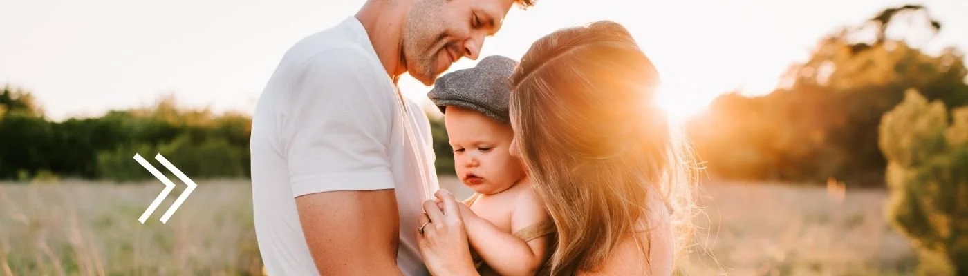 A family of three enjoying a moment outdoors at sunset, with the father, mother, and their young child.