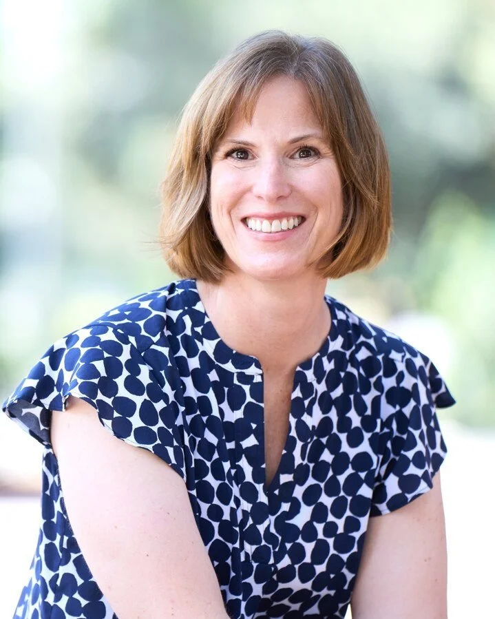 Woman sitting, smiling in a blue shirt.