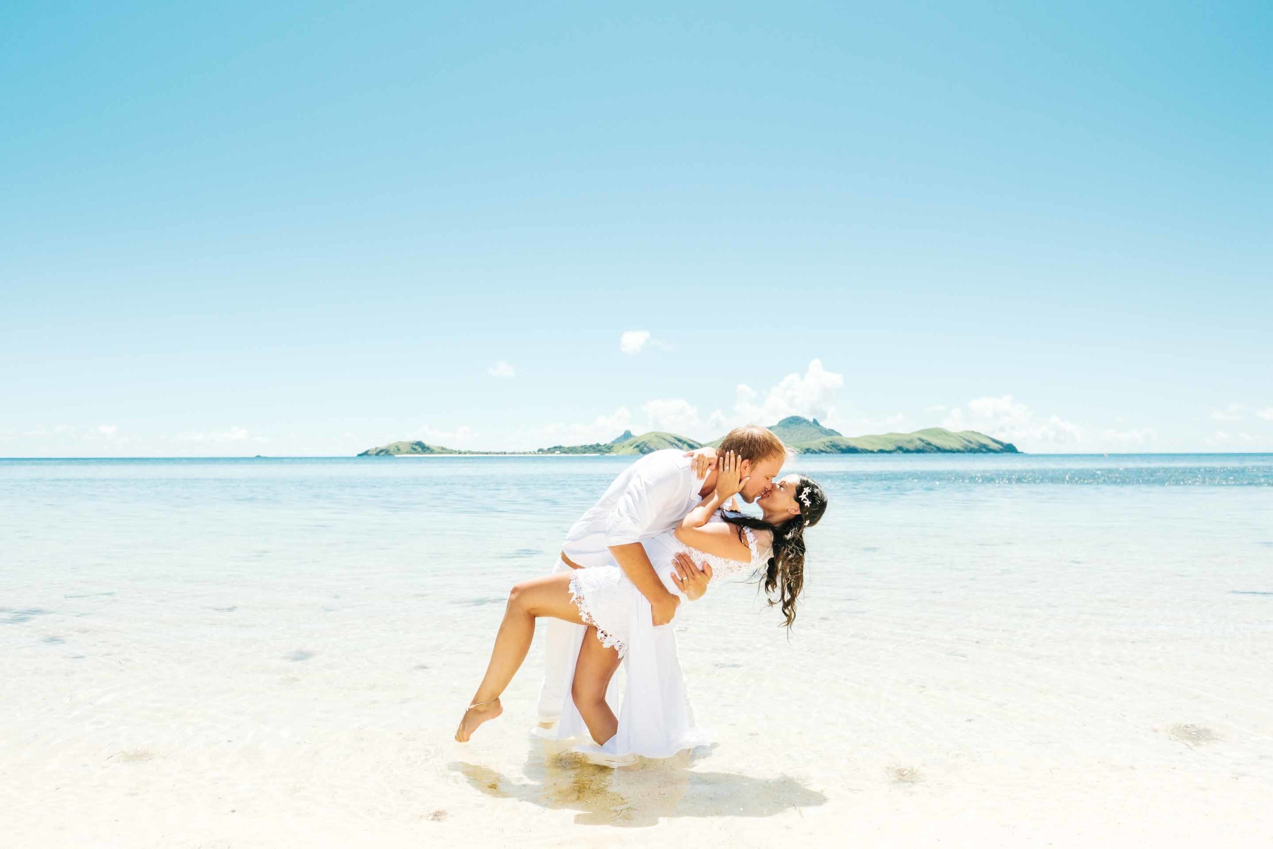 the groom dipping the bride and kiss her as they stand ankle deep in the crystal clear waters of the Mamanucas
