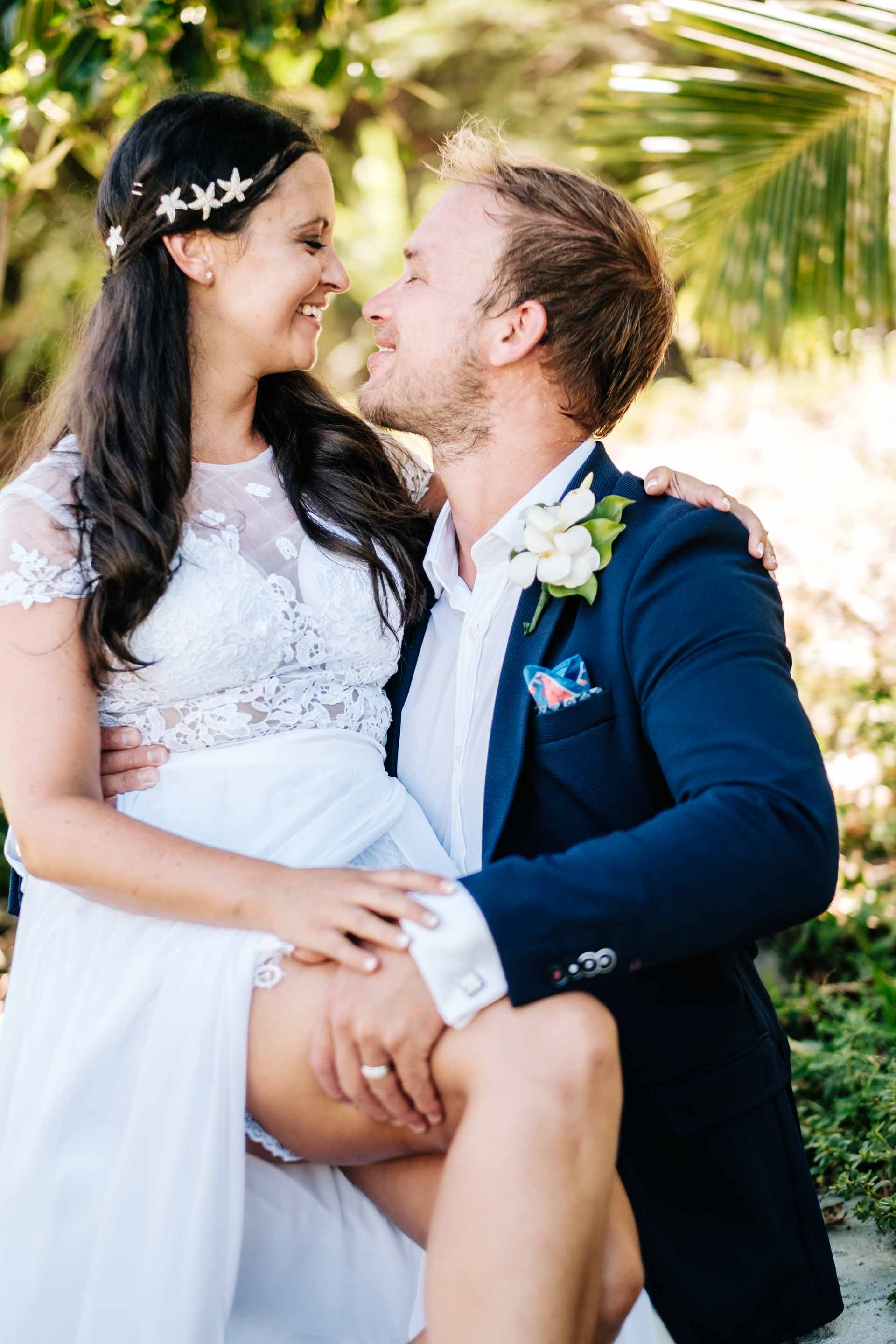 the couple sharing a moment int the resort gardens with the bride sitting on the grooms knee