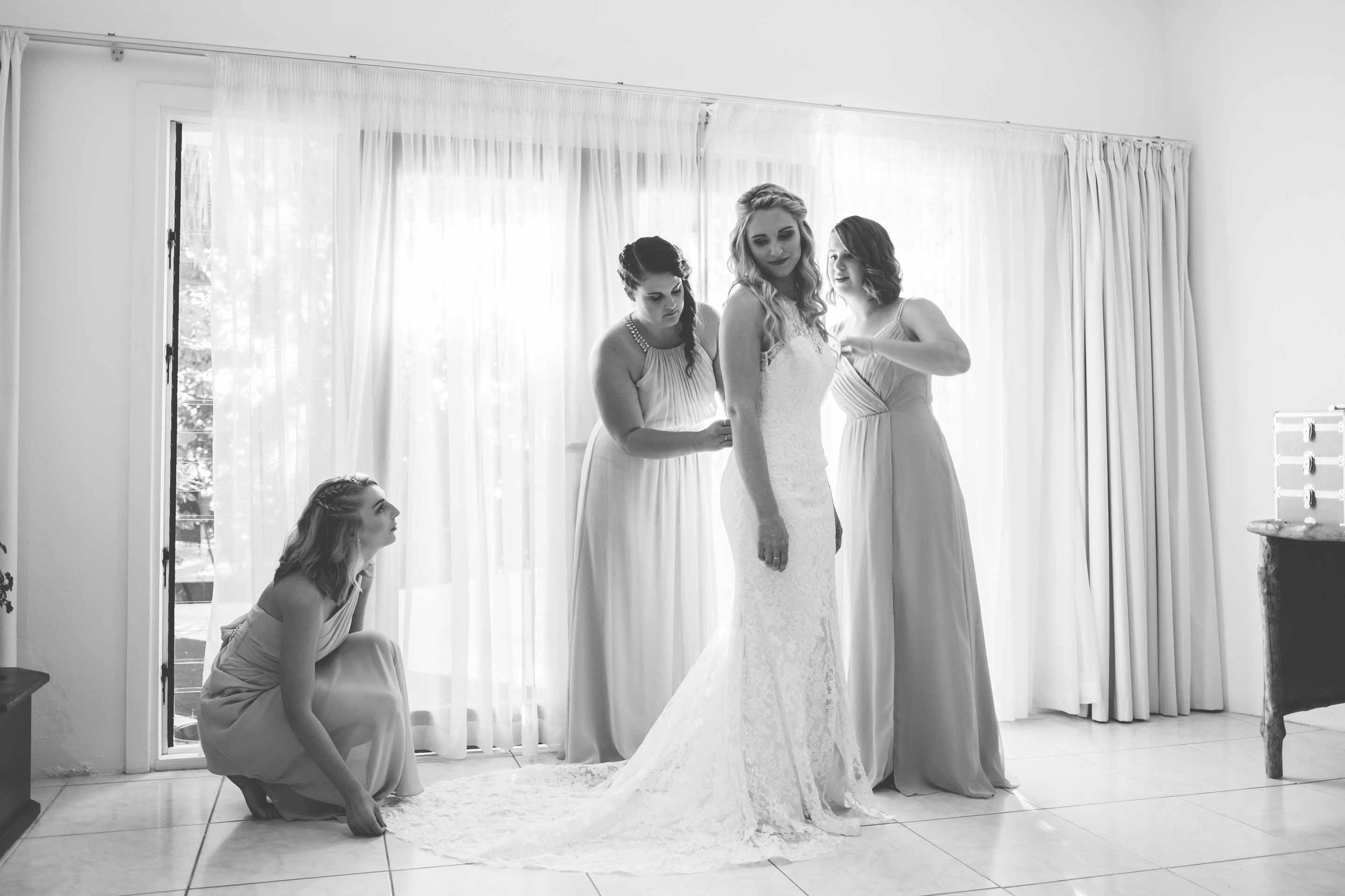 bridesmaids helping the bride into her wedding dress