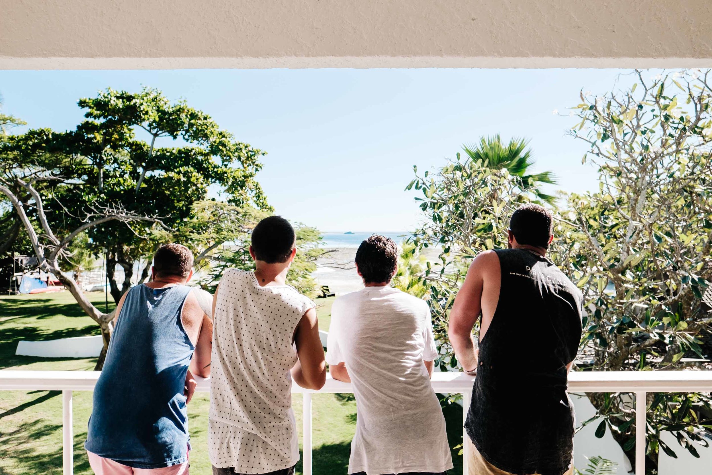 the groom and groomsmen sharing a beer while enjoying the view from their ocean view room