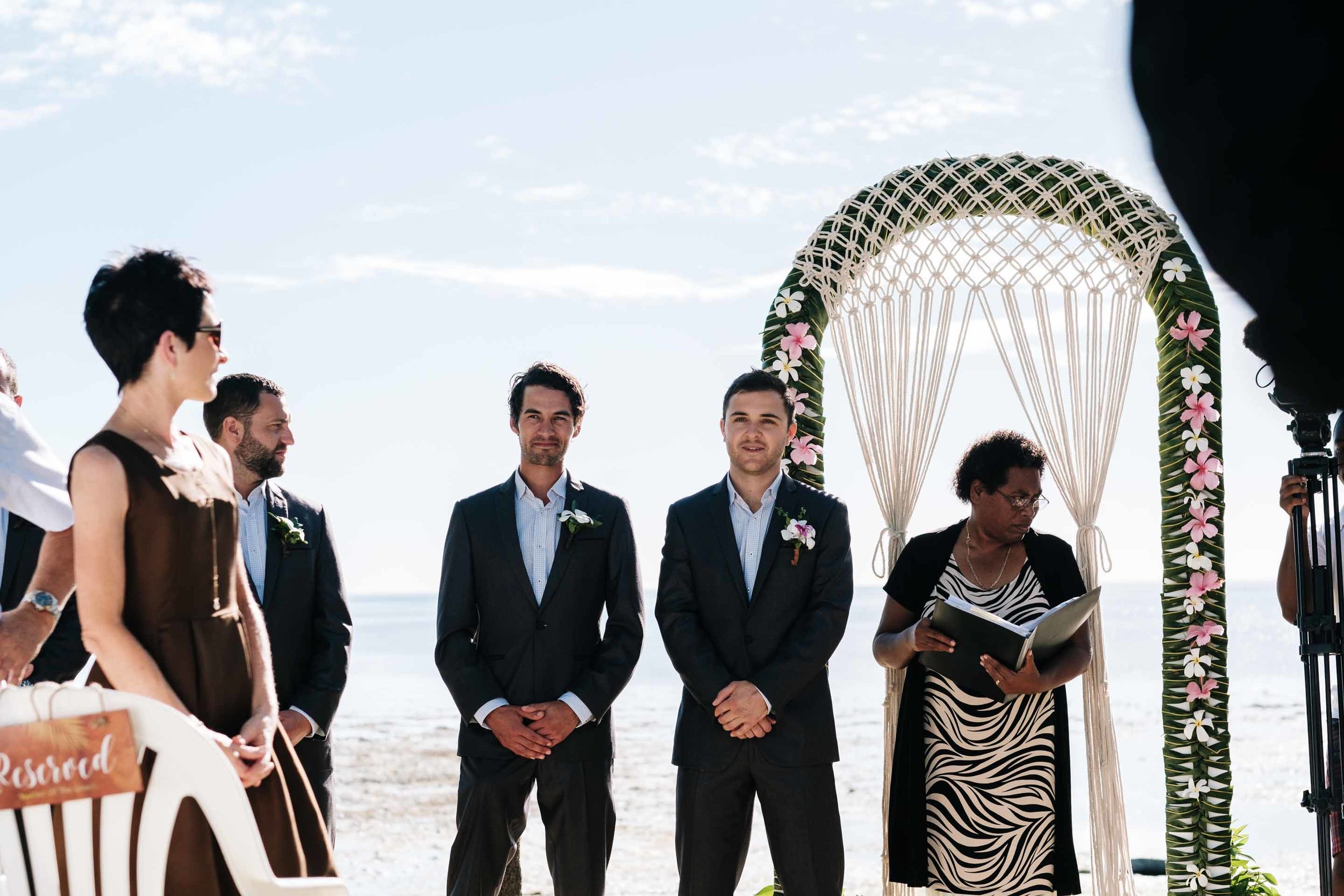 the groom at the wedding arch looking down the aisle waiting for his bride