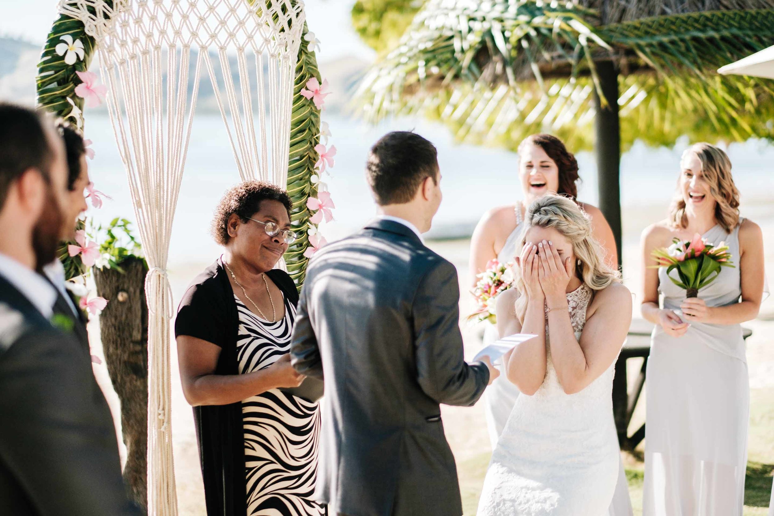 the bride reacting to the grooms vows by covering her face as she laughs