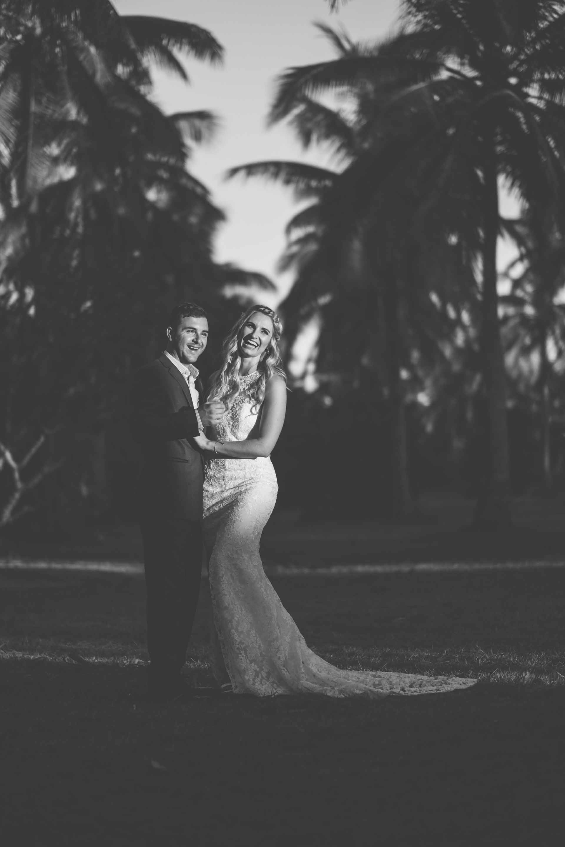 full length portrait of the bride and groom between rows of coconut trees in black and white