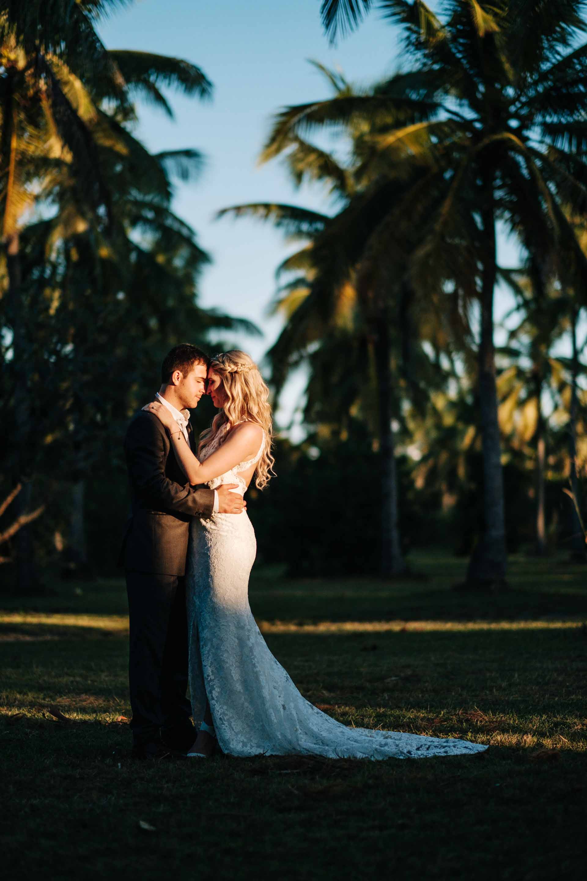 full length portrait of the bride and groom resting their bodies together between rows of coconut trees