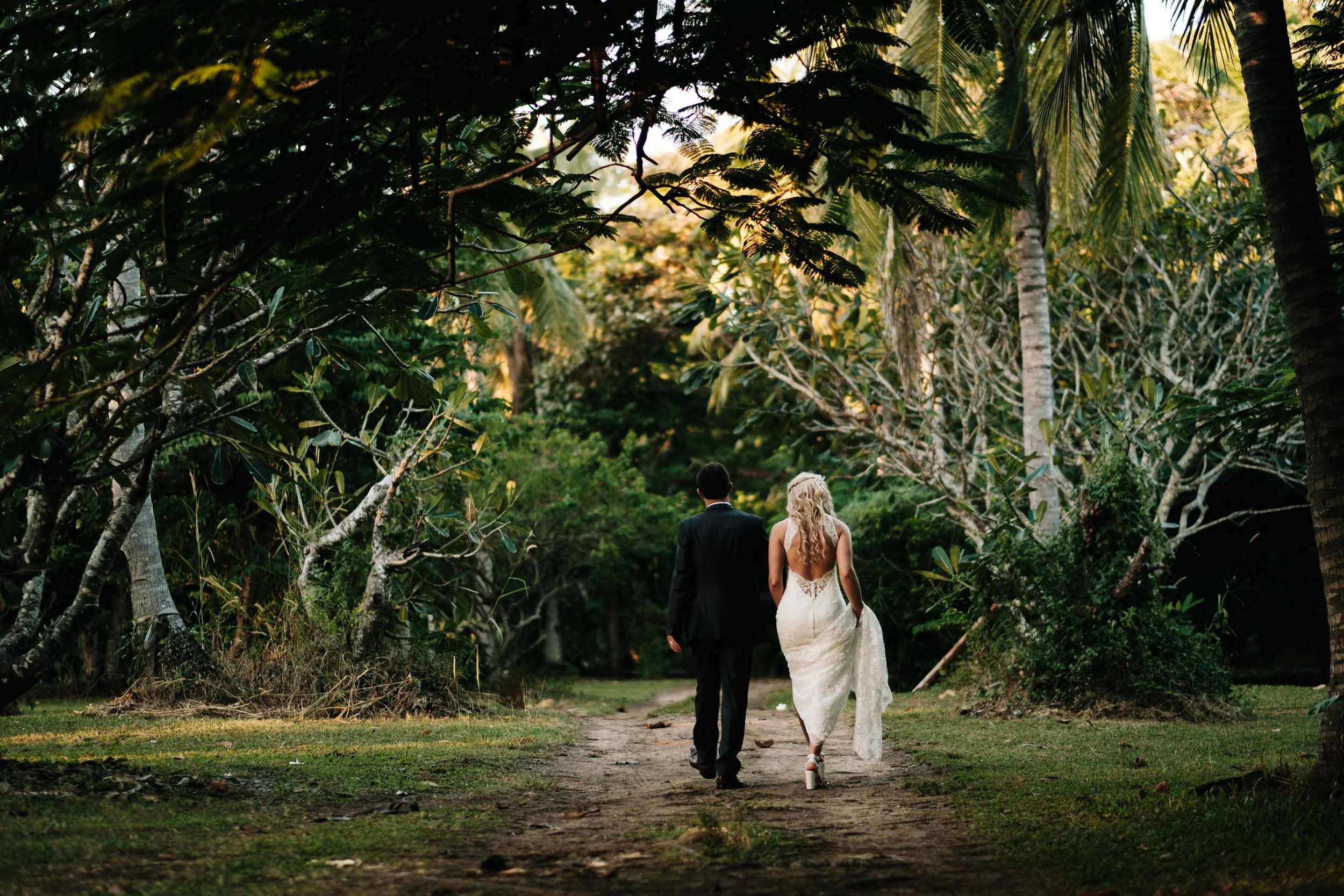 the bride and groom walking away together hand in hand under trees on a sandy dirt road