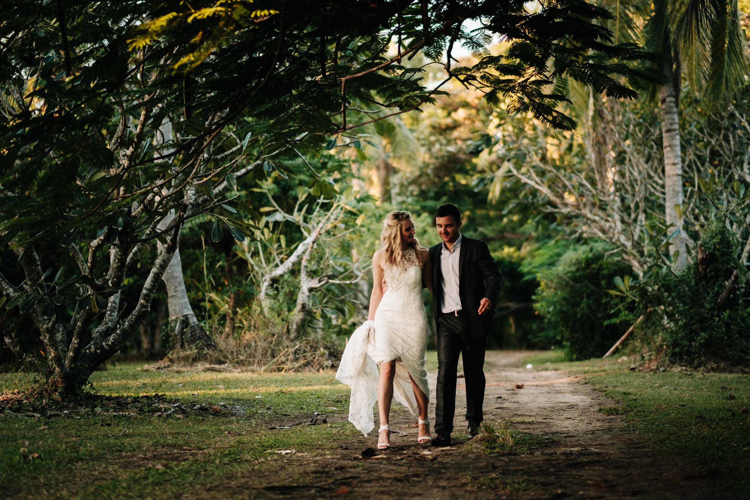 the bride and groom walking together hand in hand under trees on a sandy dirt road