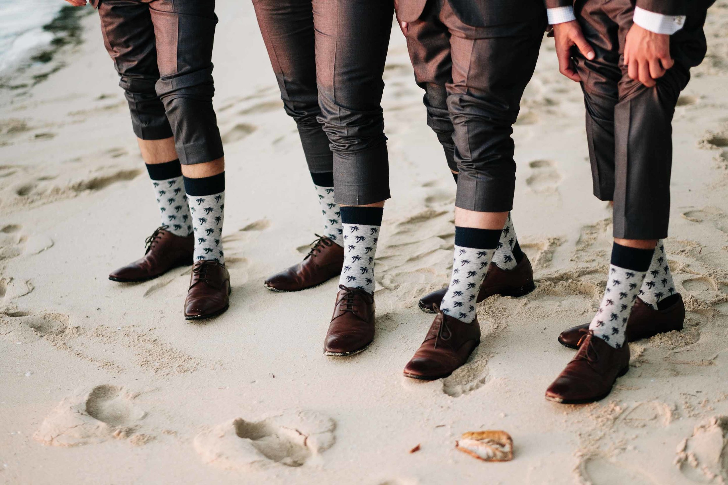 the groomsmen showing off their coconut tree socks on the white sand beach in front of the Resort