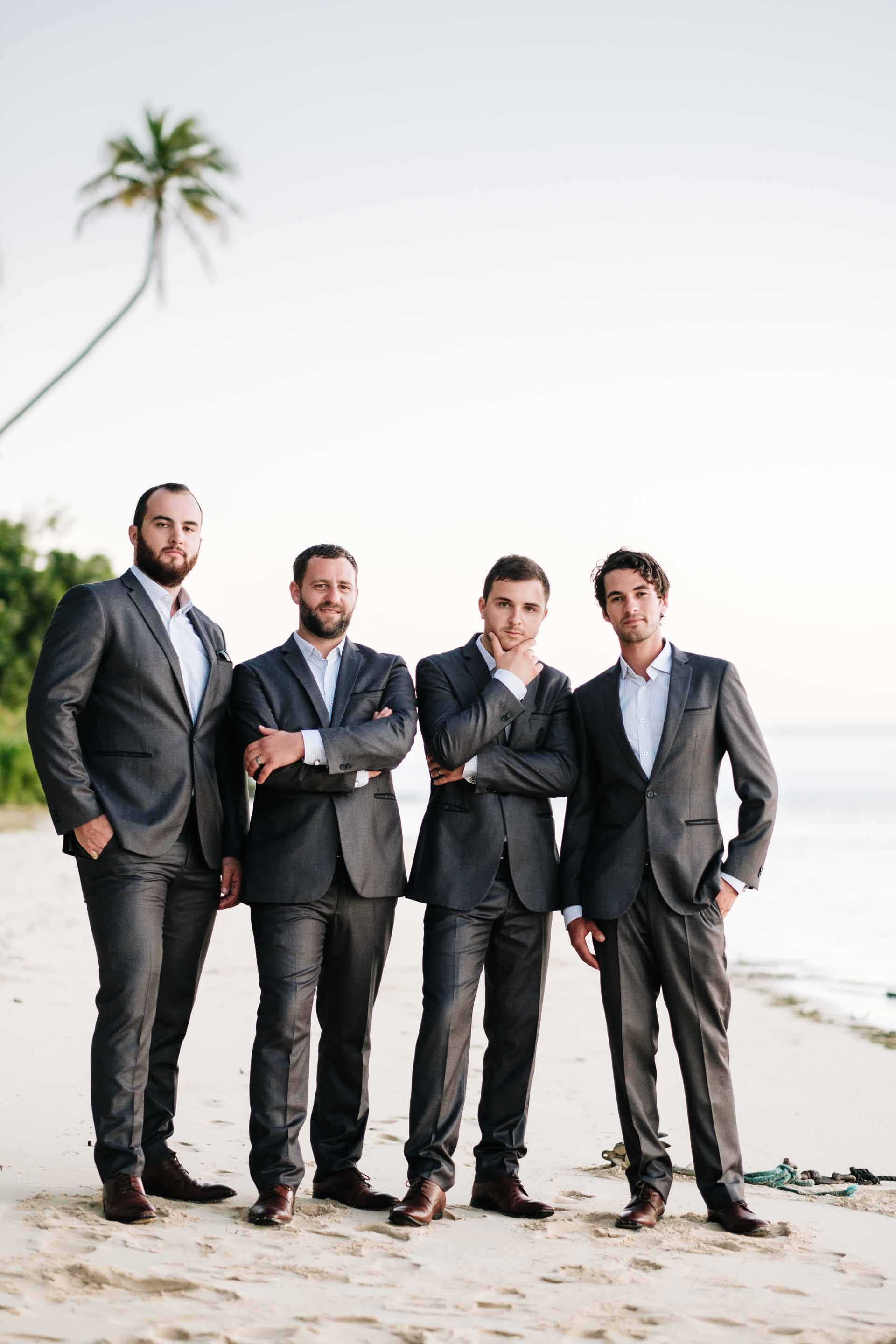 the groom and his groomsmen looking very suave on the beach at sunset