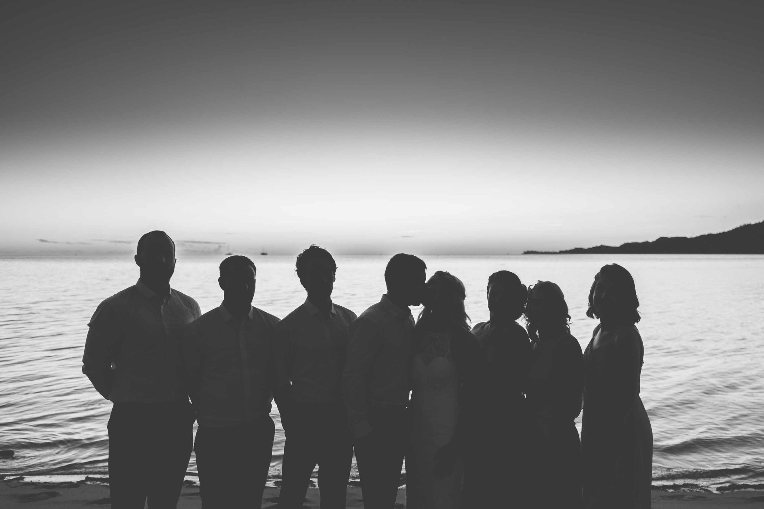 the bridal party silhouetted against the calm warm seas just after the sun has set in black and white