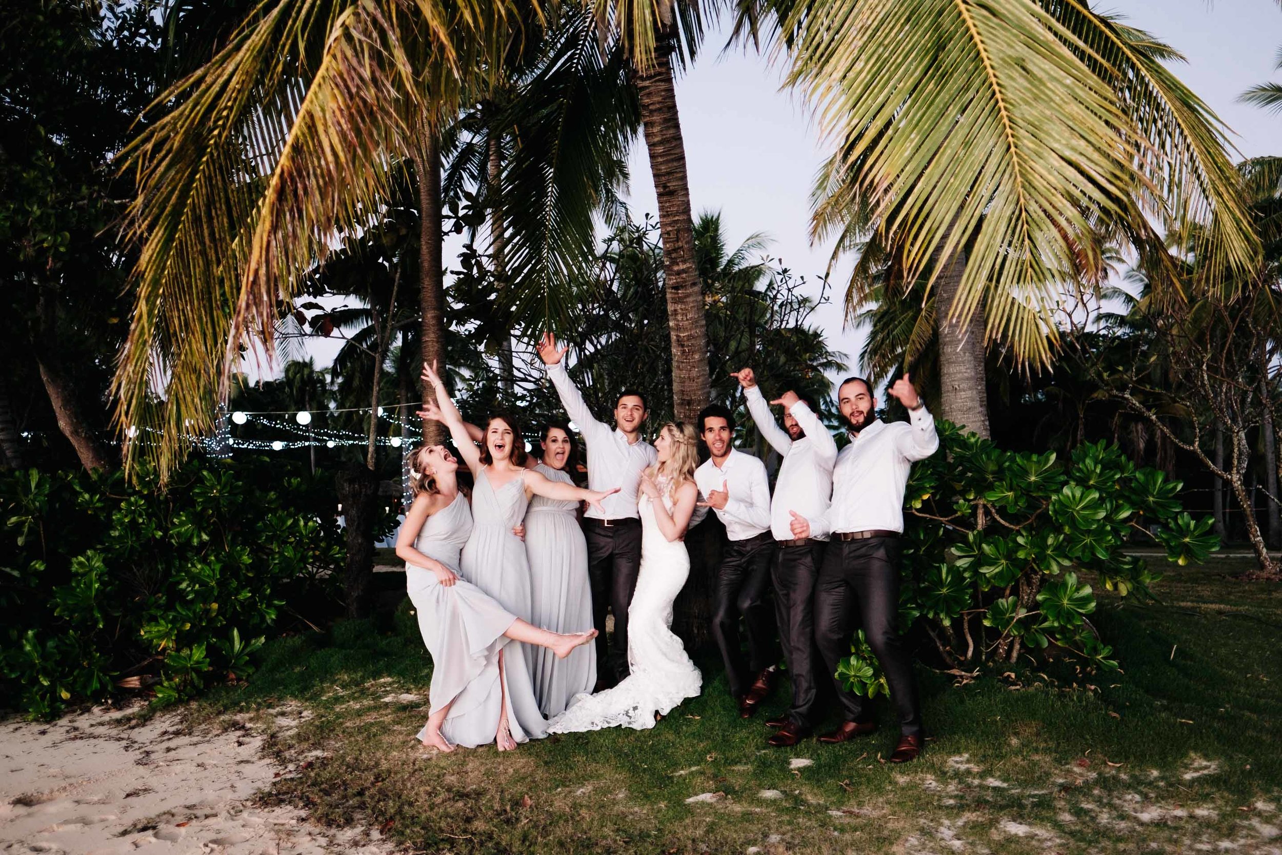 the bridal party having a light moment under a coconut tree next to the beach