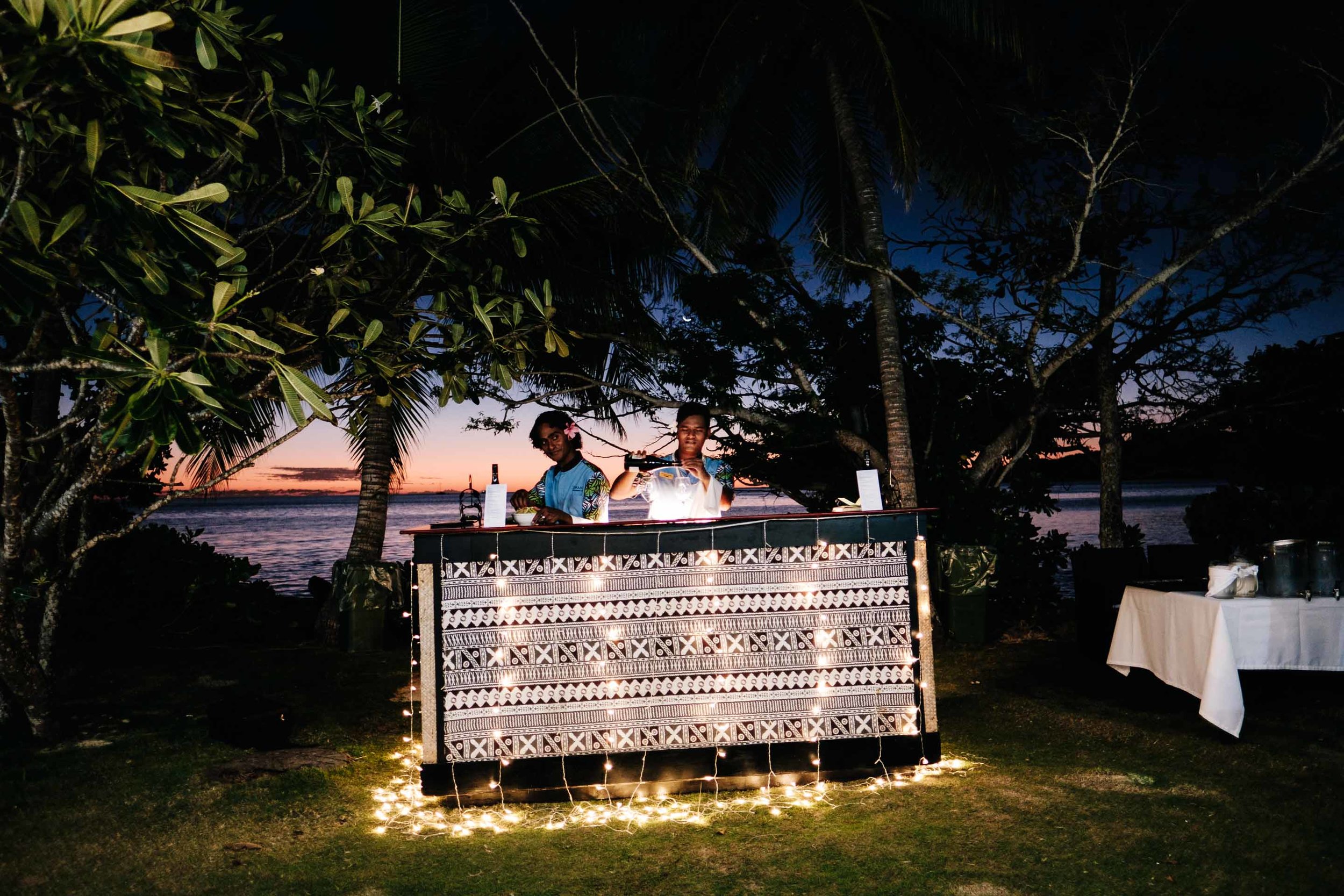 the bar staff mixing drinks behind the outdoor bar with traditional tapa print and surrounded by fairy lights