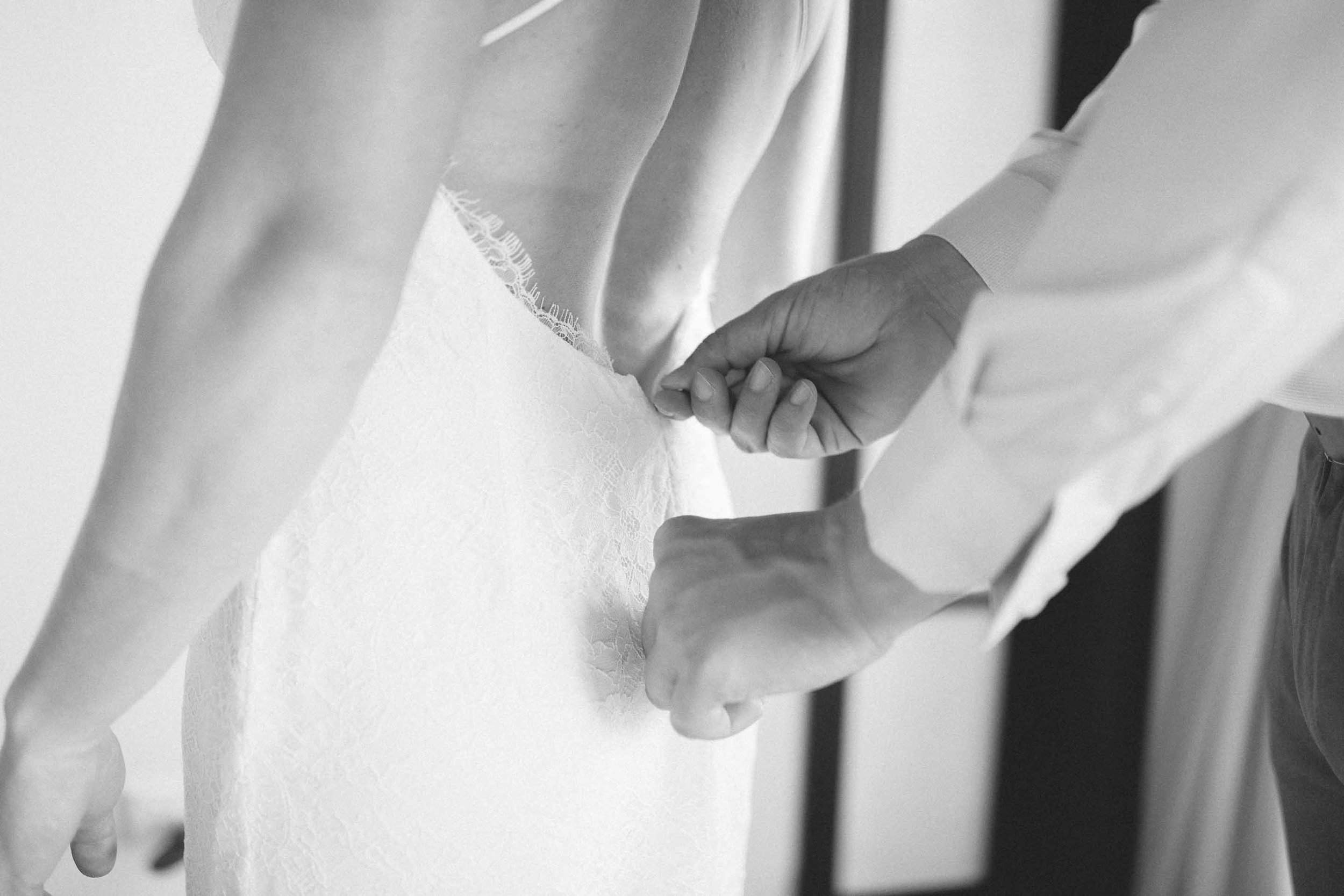Groom helps the Bride zip up her wedding dress