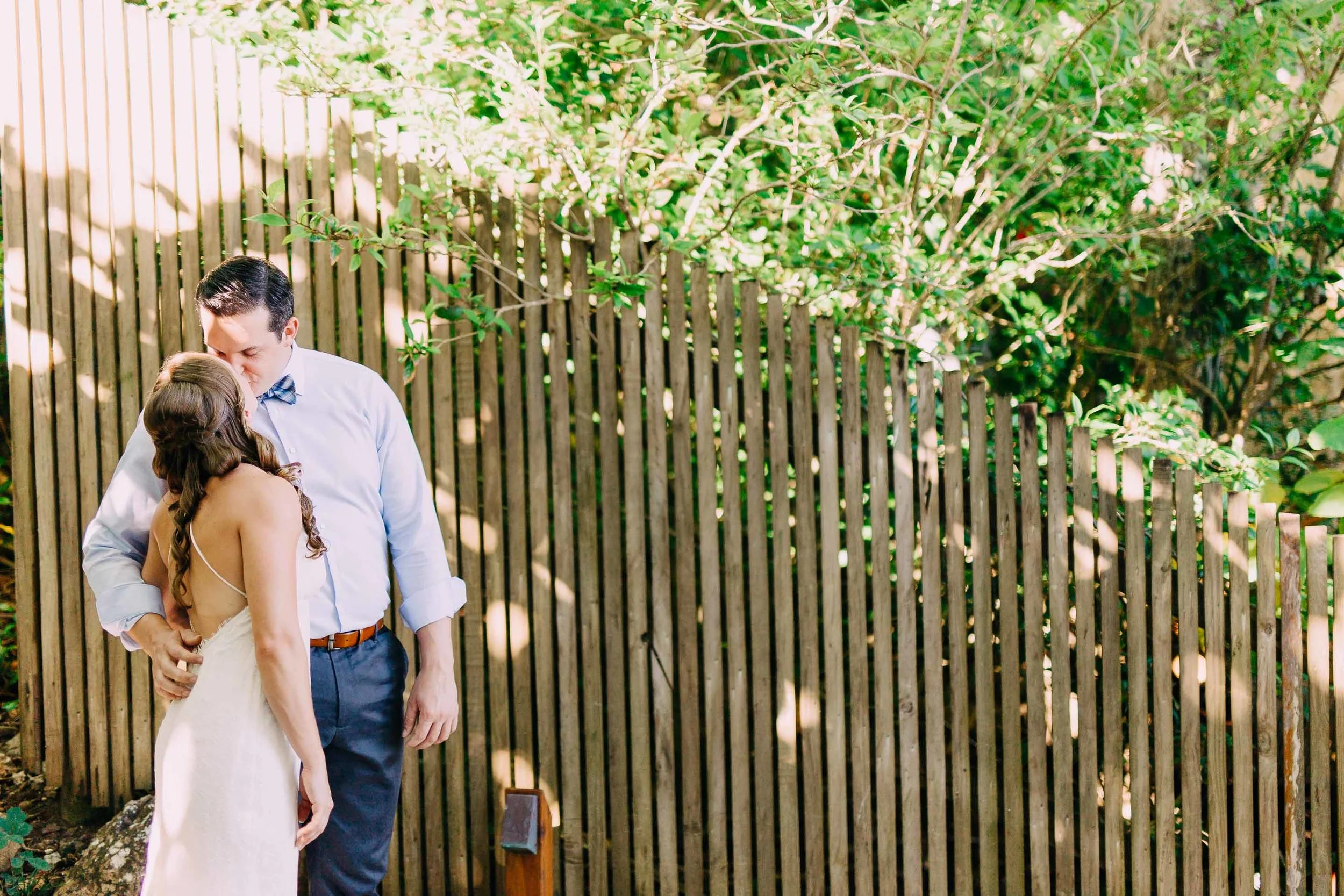 Fiji bride and groom kiss in front of a bamboo wall.