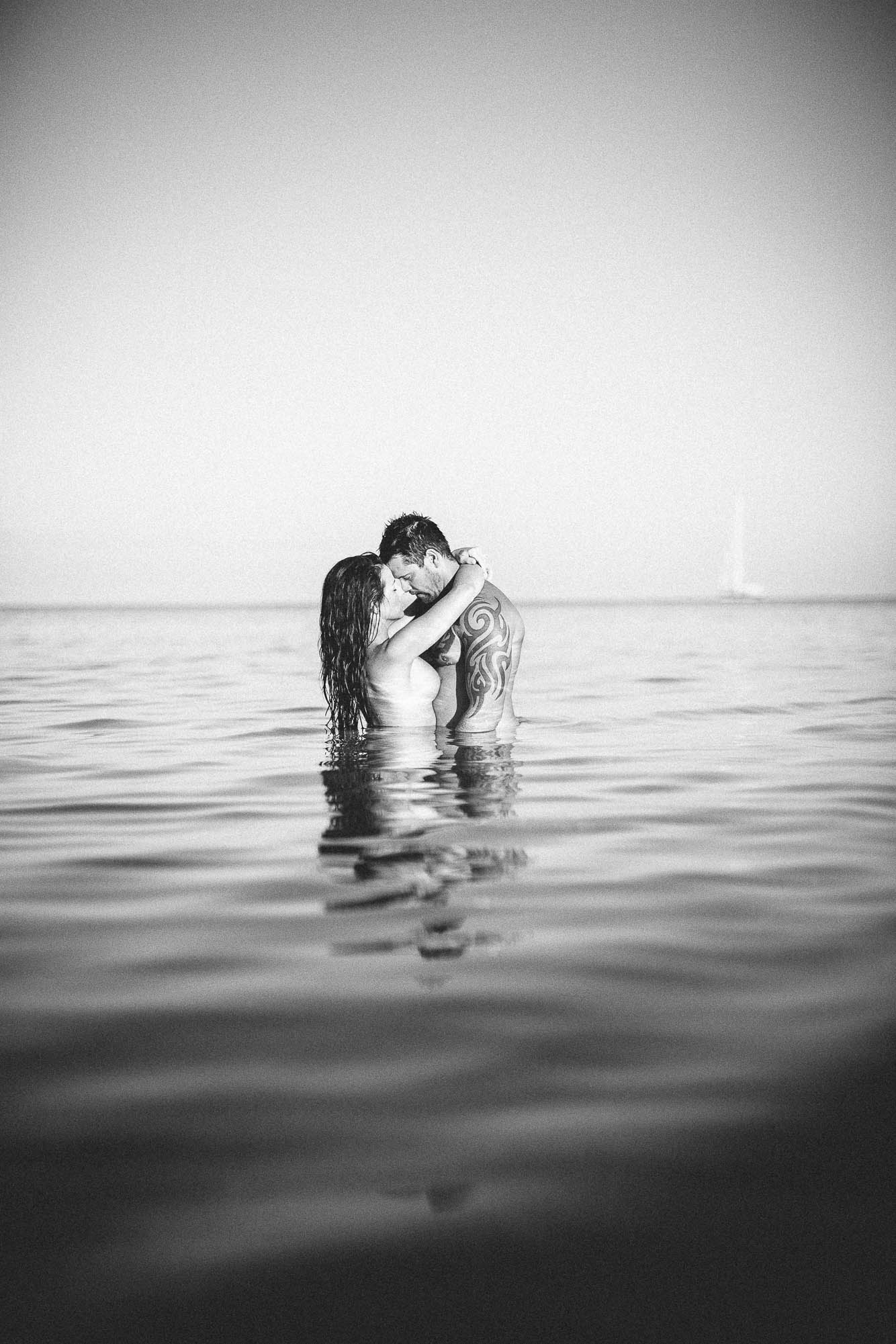 Bride and groom kissing topless in the sea
