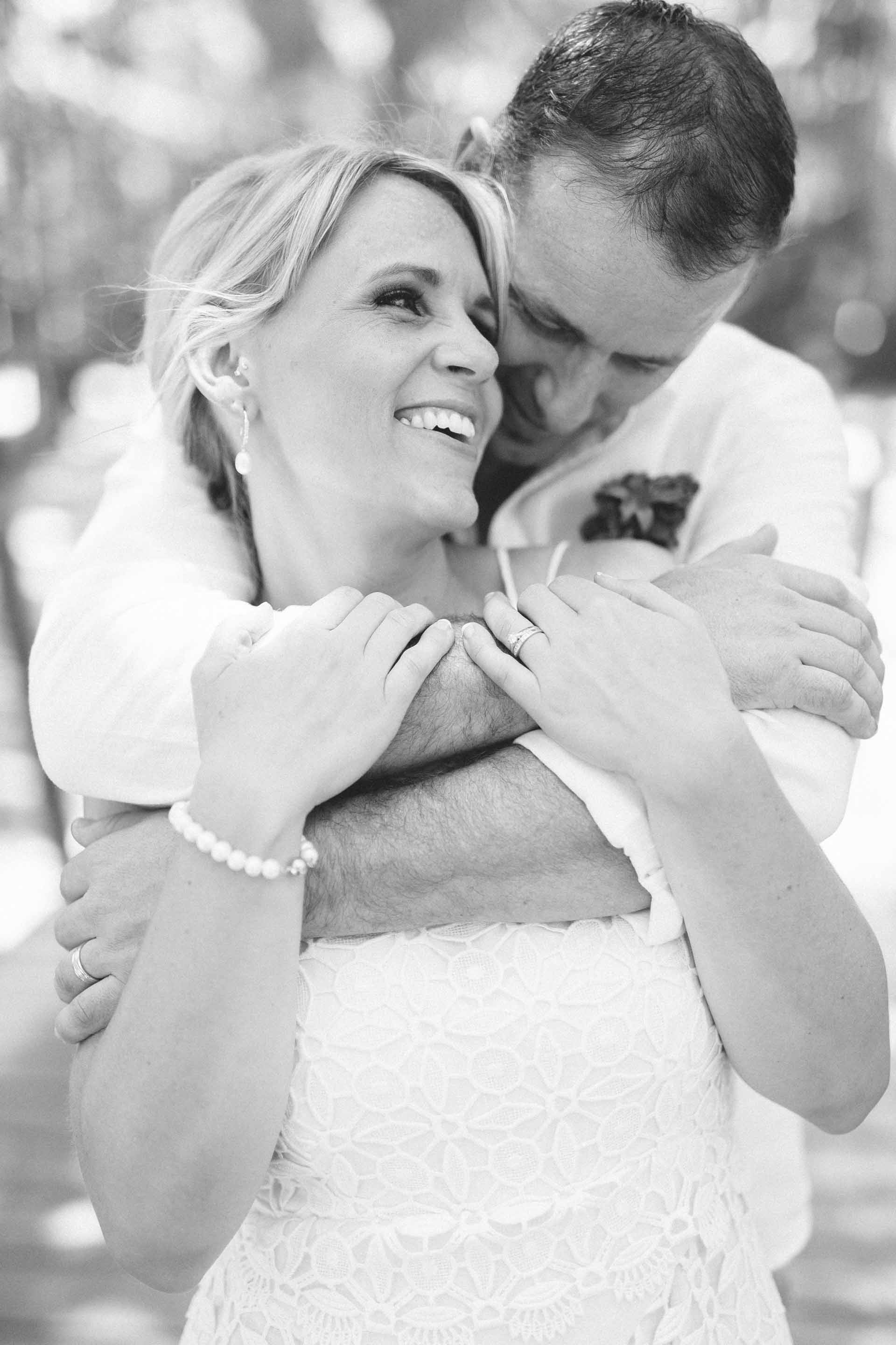 the groom hugs the bride from behind in black and white