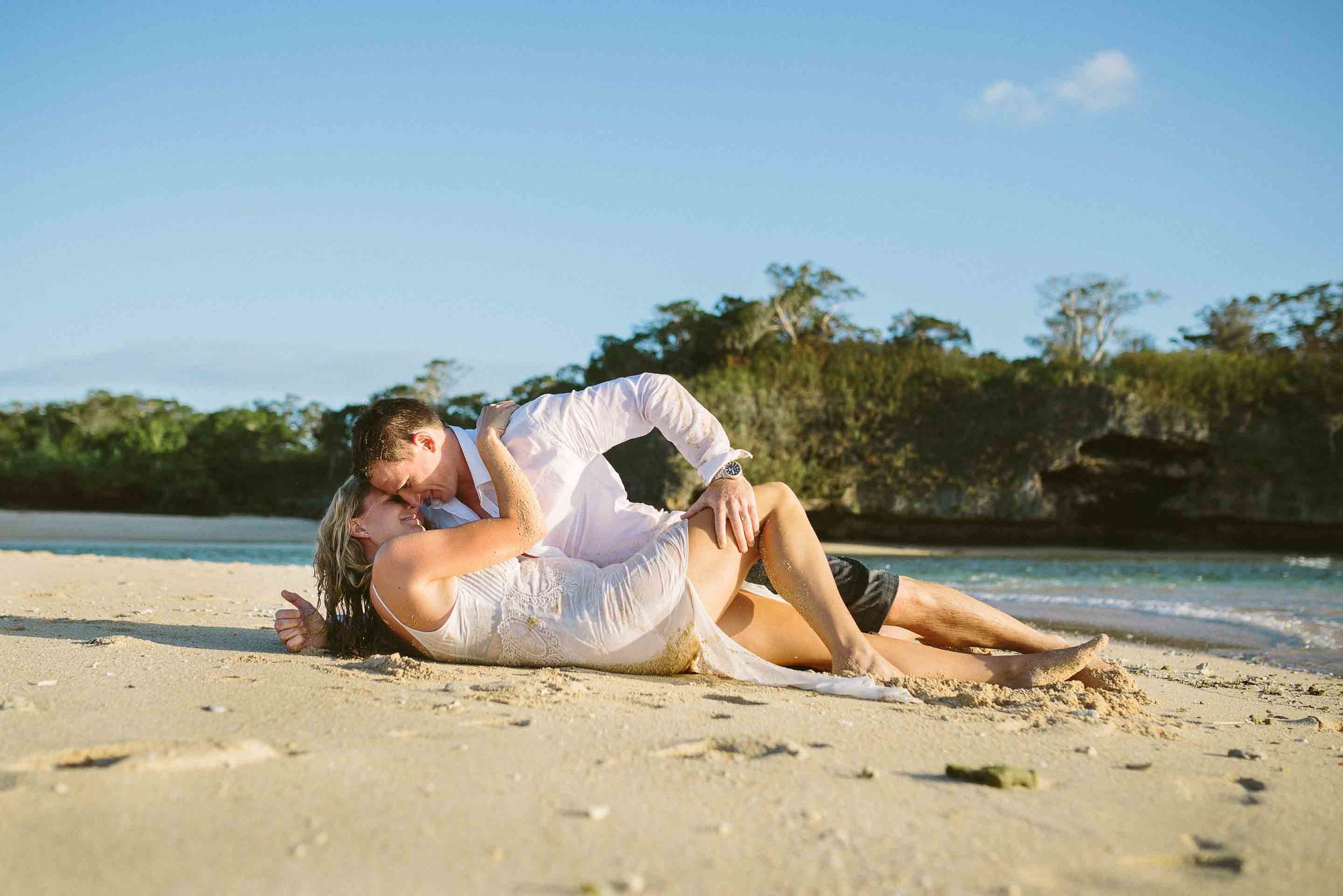 groom lying on top of bride on beach