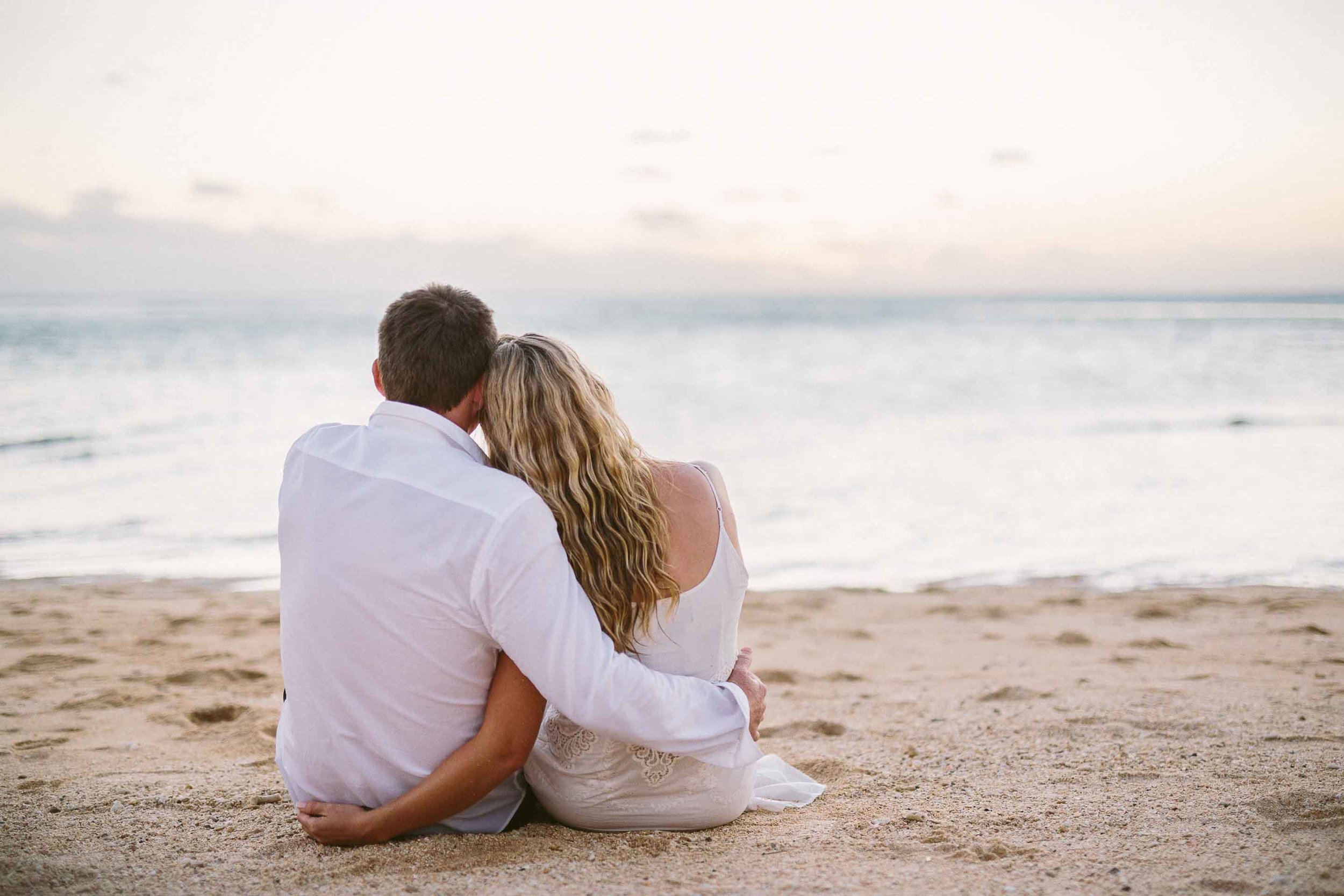 the couple holding each other as they sit on the beach watching the sunset