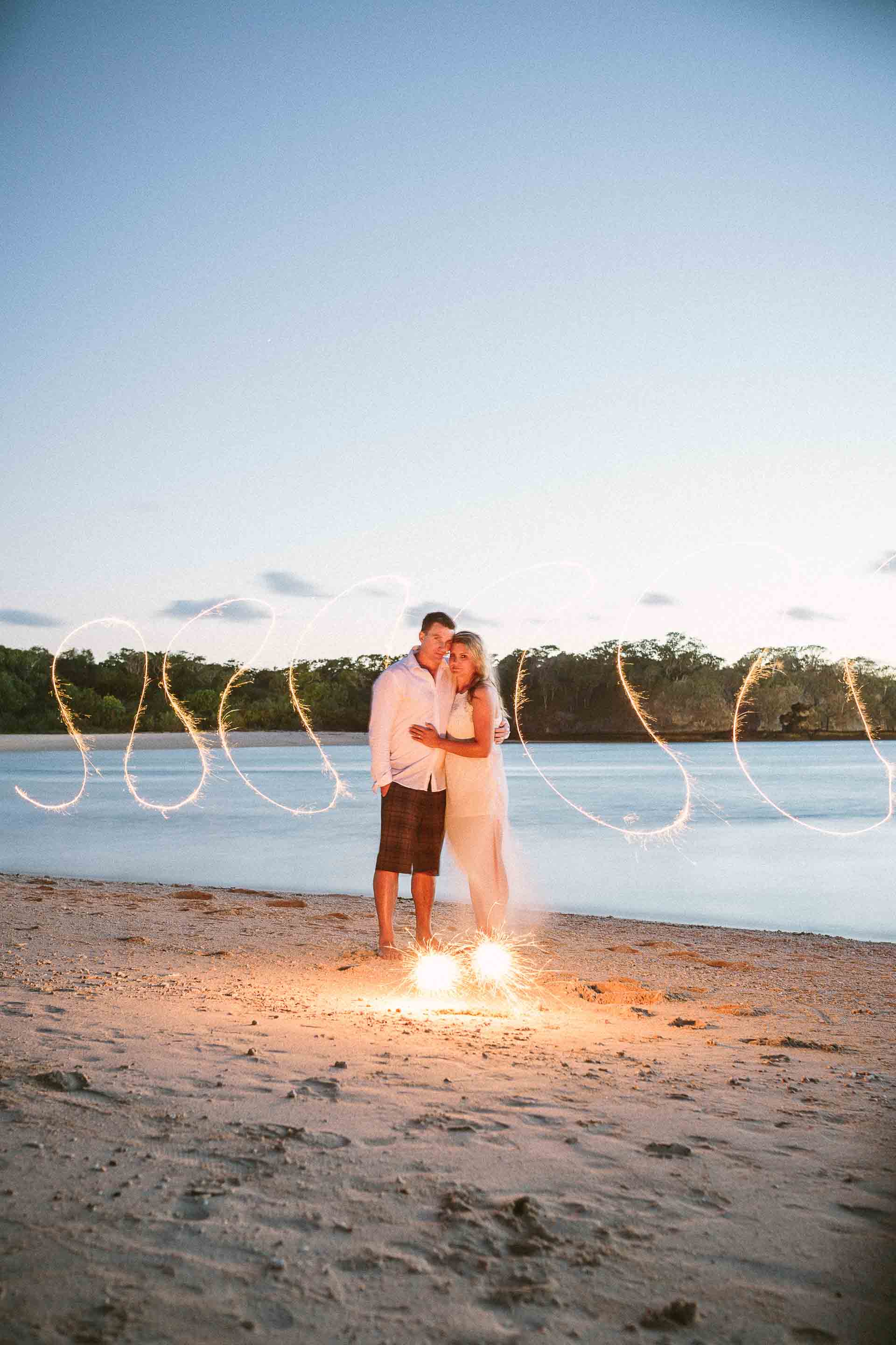 the couple standing on the beach light by sparklers