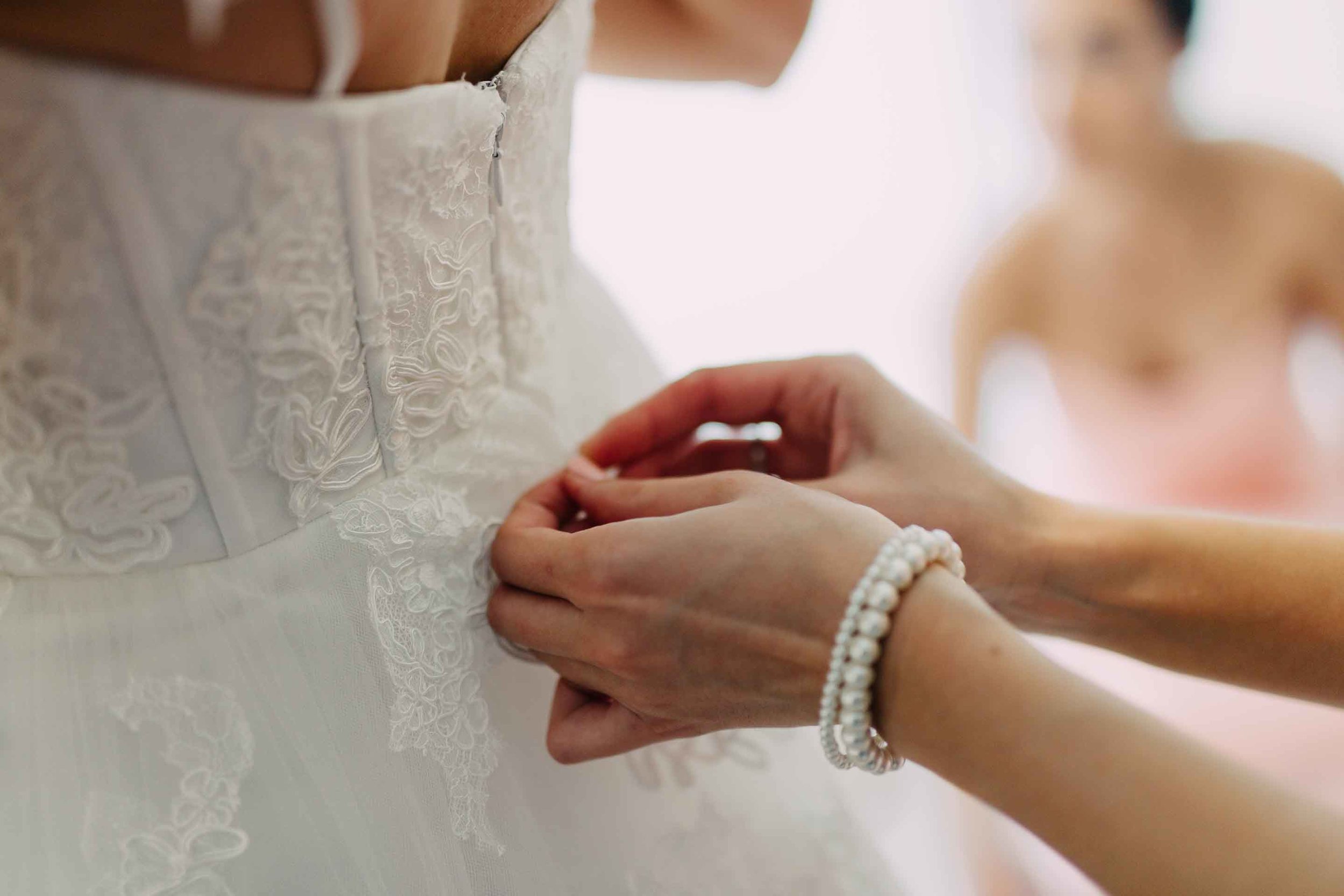 Bridesmaid helps with the back of the Bride's wedding dress.