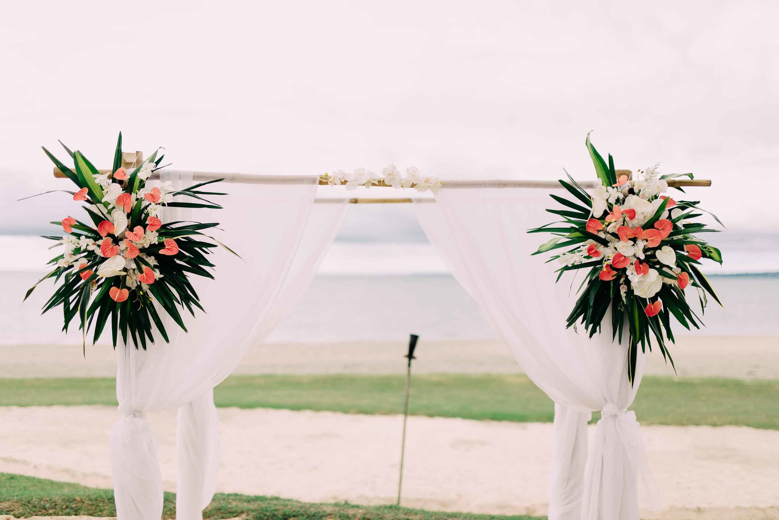 Beautiful tropical colourful flowers on a white draped bamboo wedding ceremony arch. Perfect for a Fiji beach wedding