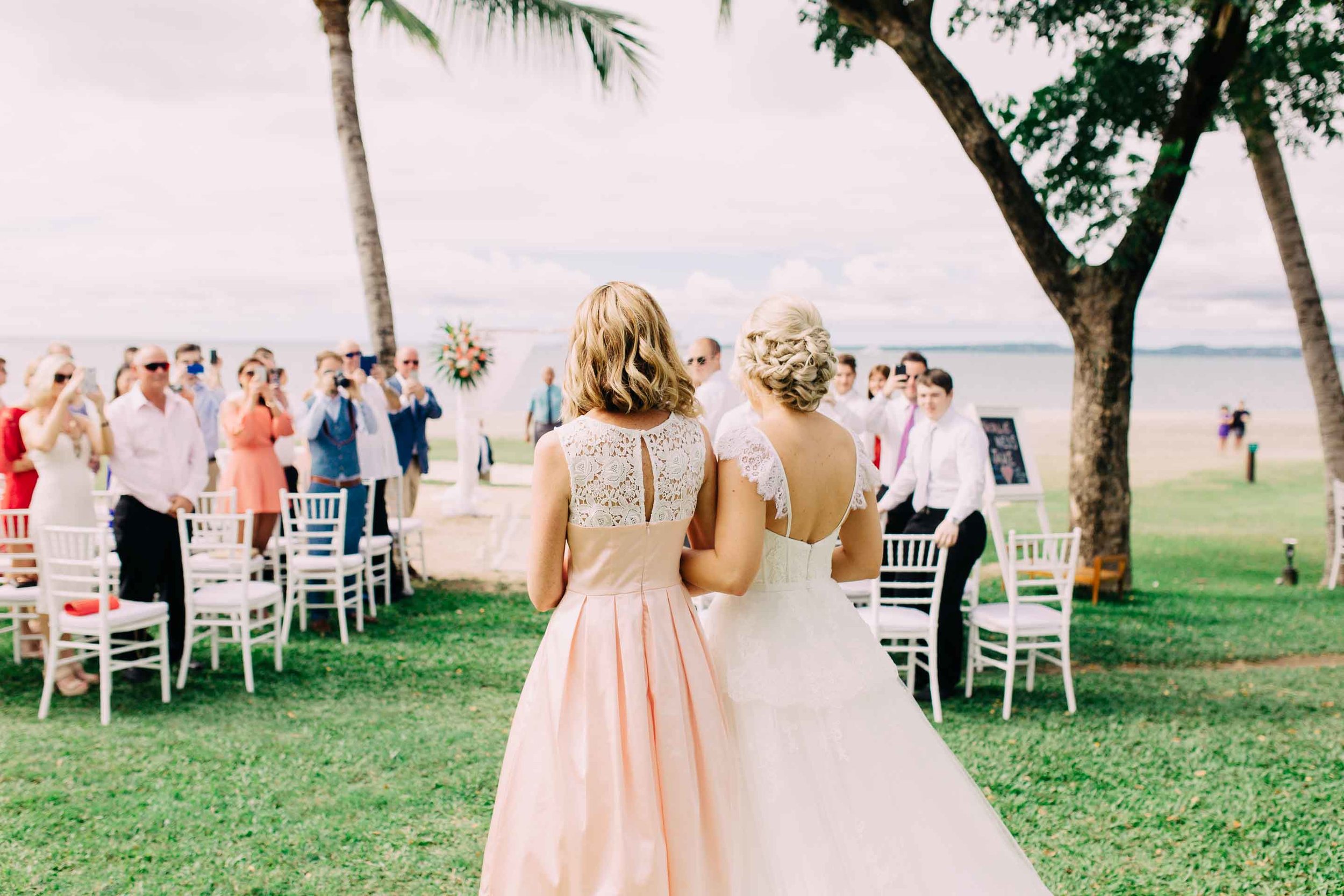 Groom watches his beautiful bride walking down the aisle with her mother. 