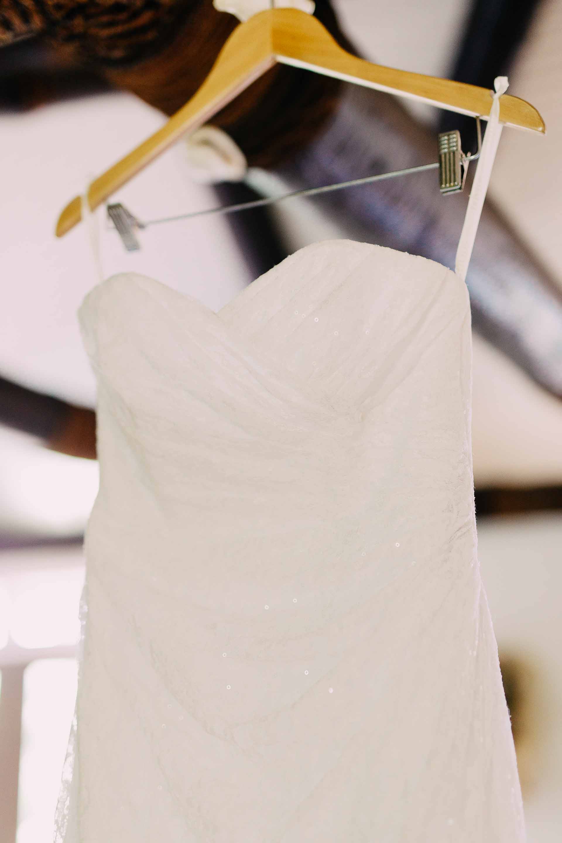 the brides dress hanging from a beam on a wooden hanger