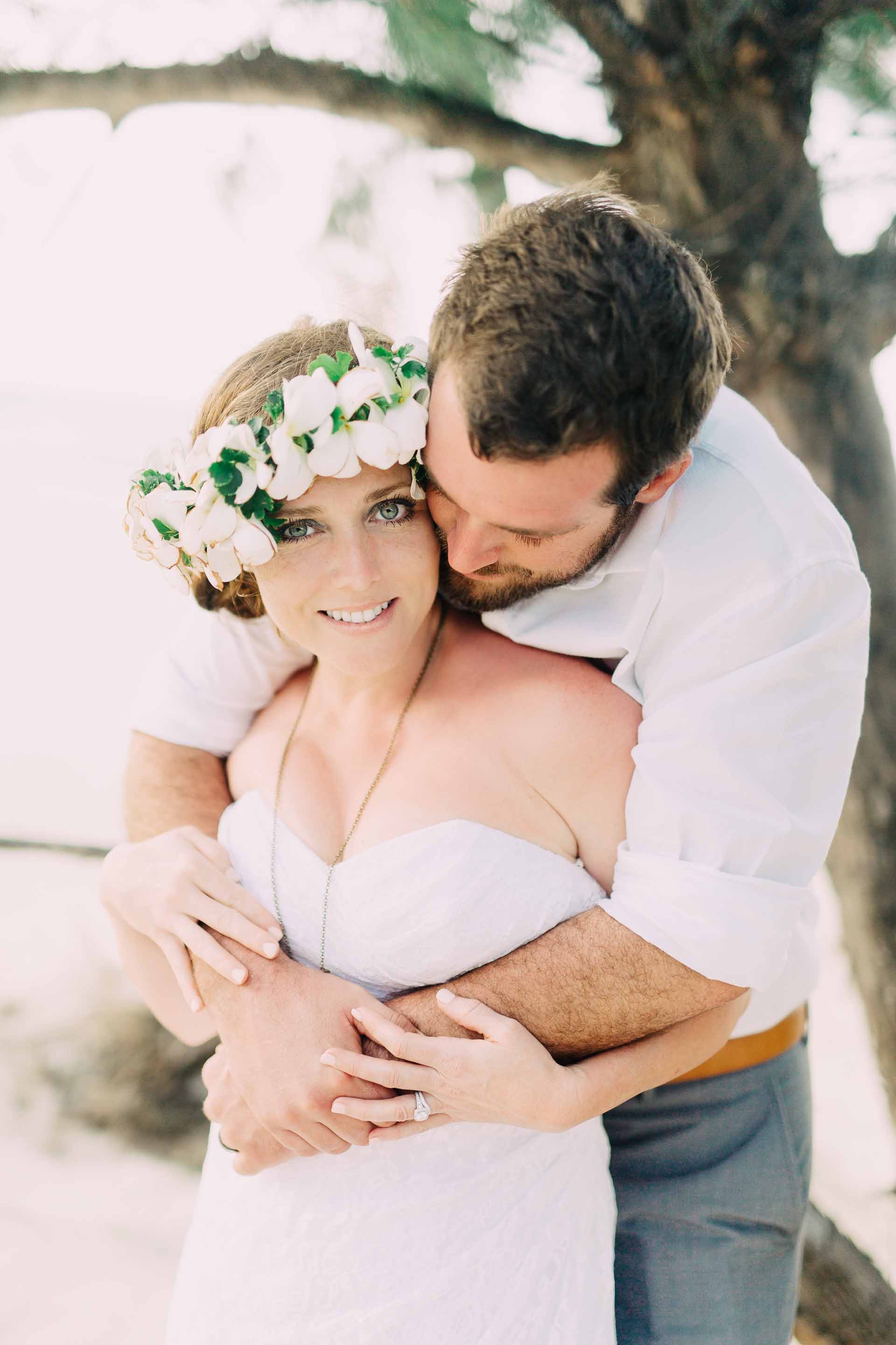 the groom hugging the bride as she looks at the camera