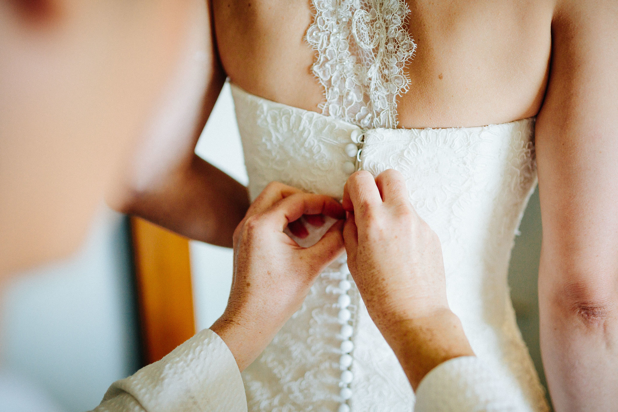 Maid of Honor buttoning up the brides wedding dress.