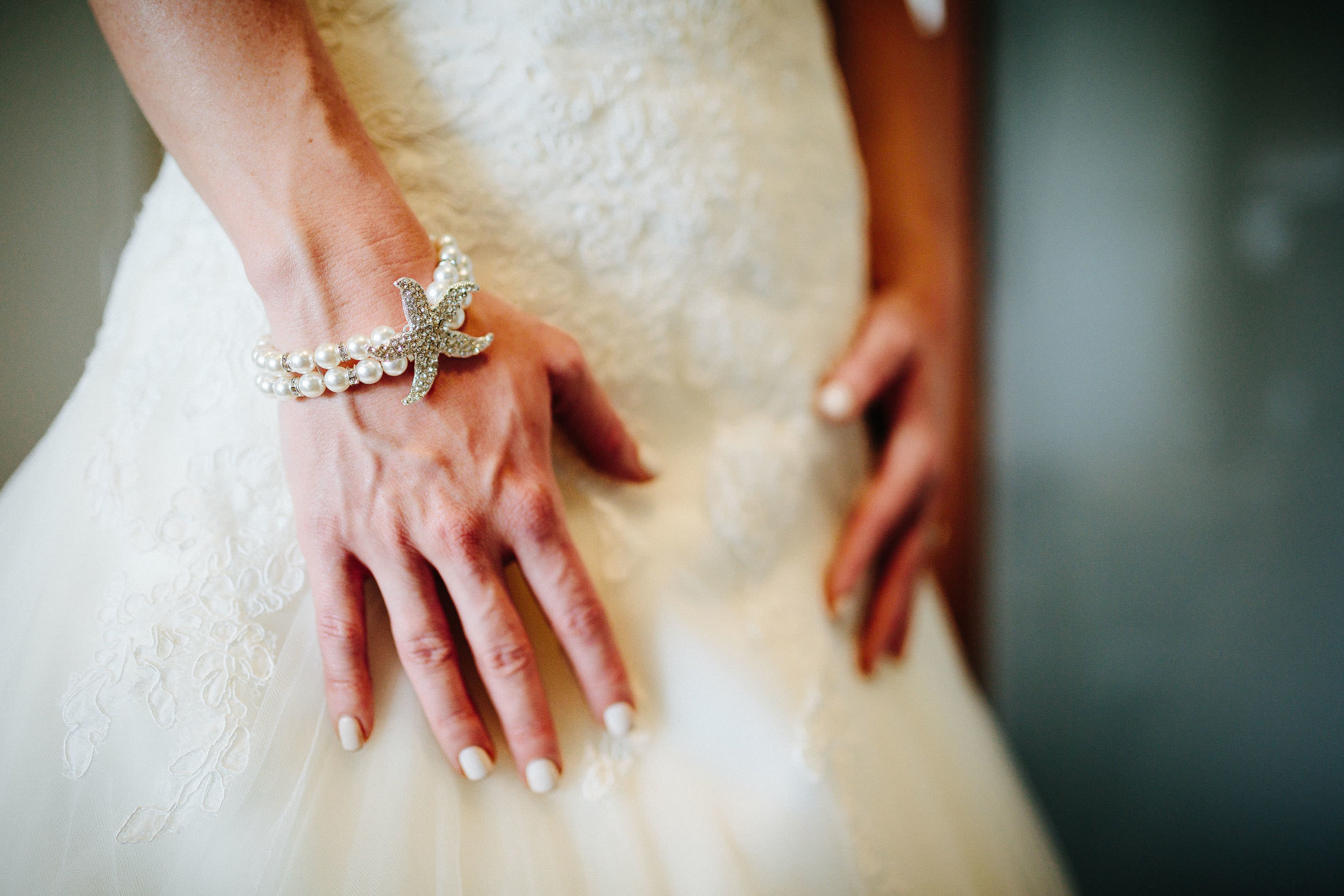 The brides hands resting on her dress with her jewellery on.