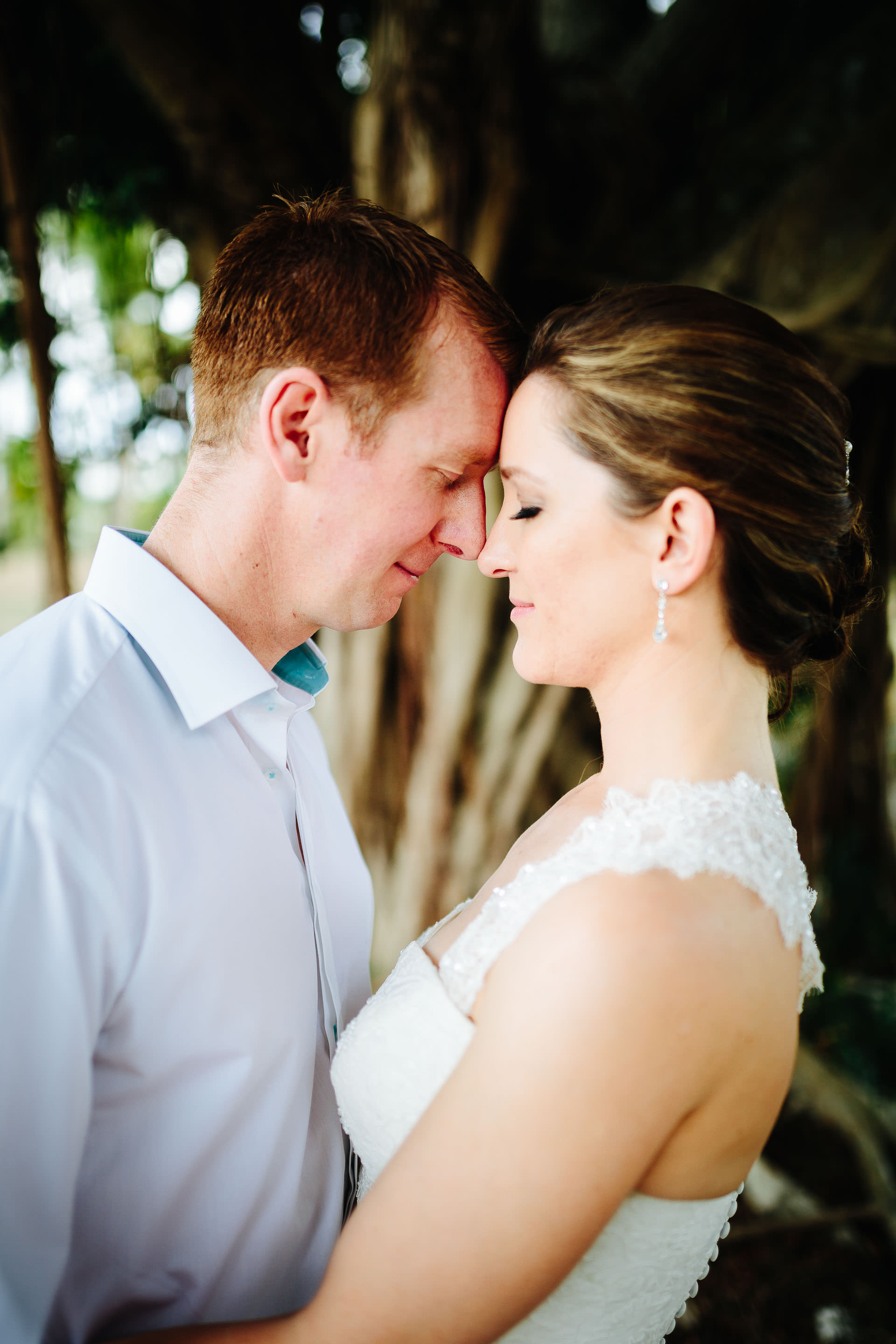 The bride and groom pose for a photo under a tree