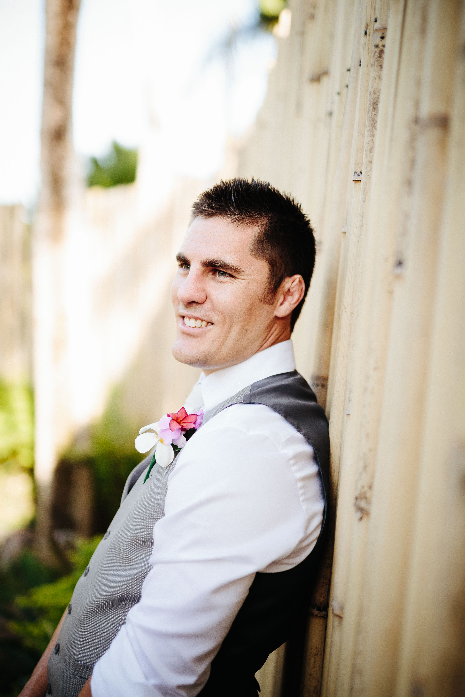 groom leaning against bamboo fence